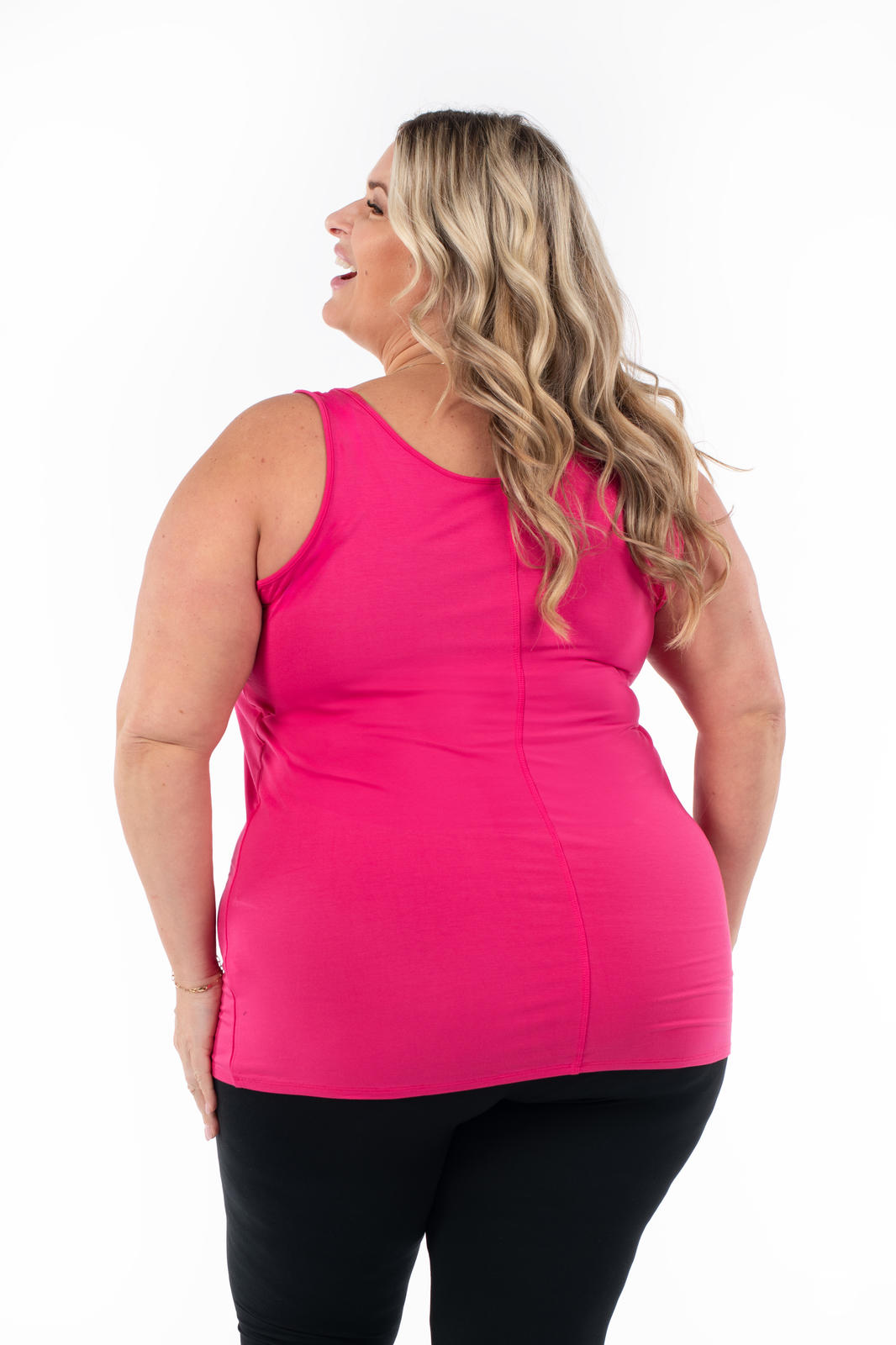 Plus size woman smiling and looking sideways wearing bright raspberry Classic Layering Tank by SweetLegs Canada with black leggings