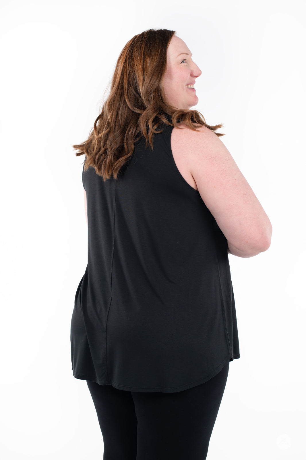 Plus-size model smiling wearing SweetTops High Neck Swing Tank in black shown from side back on white background