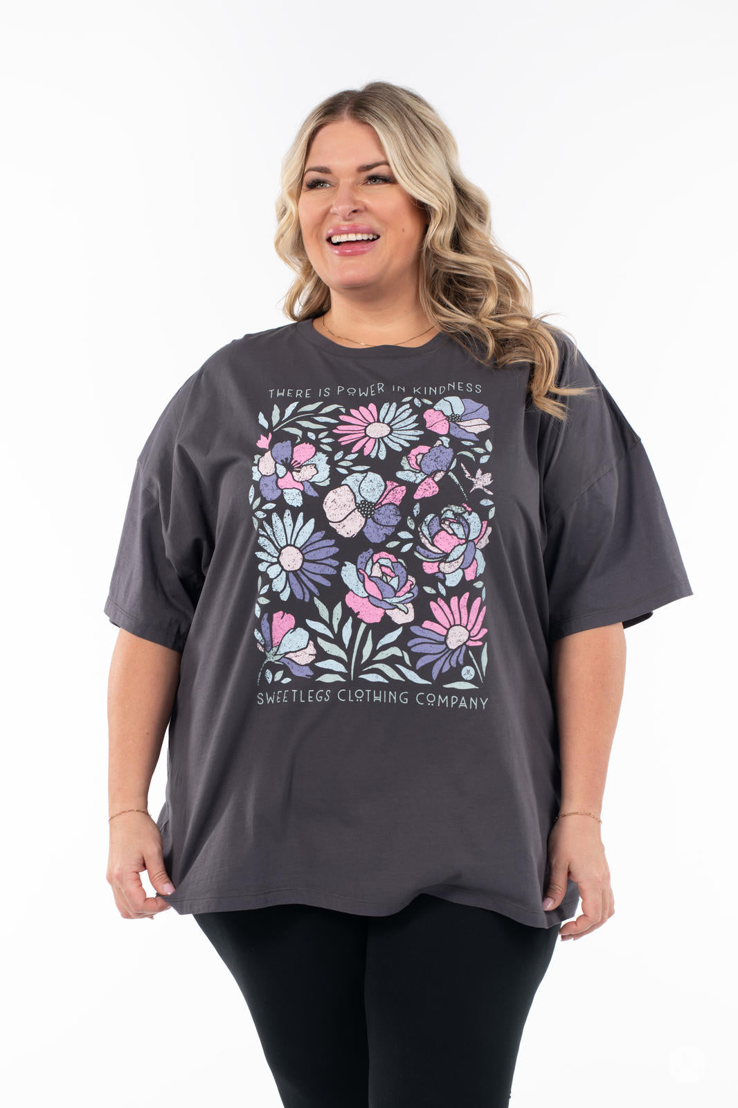 Smiling woman wearing SweetTops Vintage Graphic Tee in charcoal with colorful floral design and positive kindness affirmation