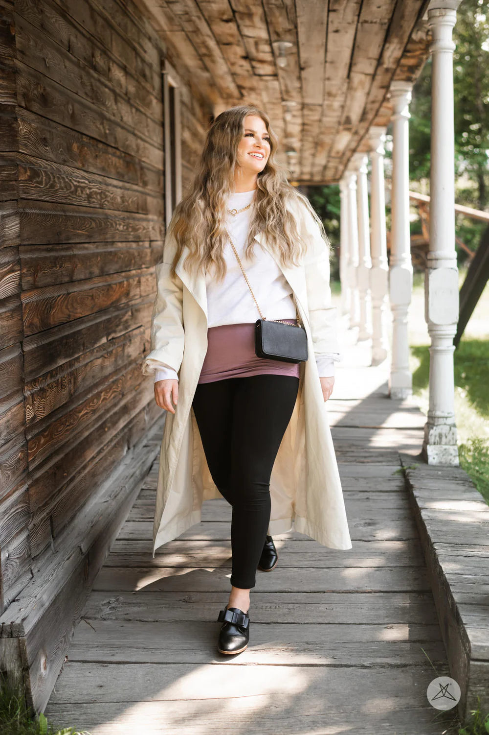 Woman walking on wooden porch wearing SweetLegs Black Licorice leggings and light coat with crossbody bag outdoors
