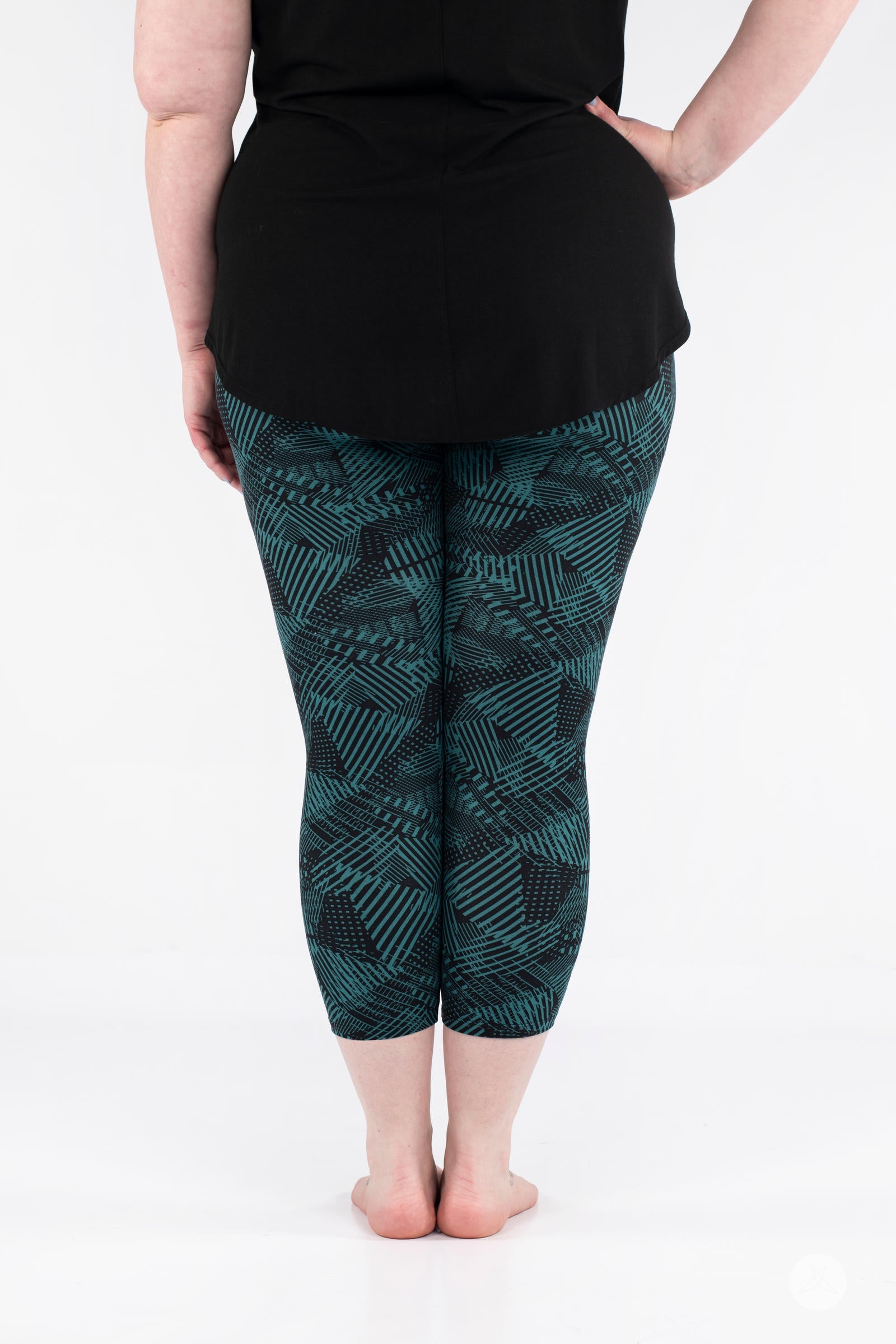 Rear view of plus size model wearing SweetLegs Geometric Glam Crops with teal and black abstract geometric cropped leggings
