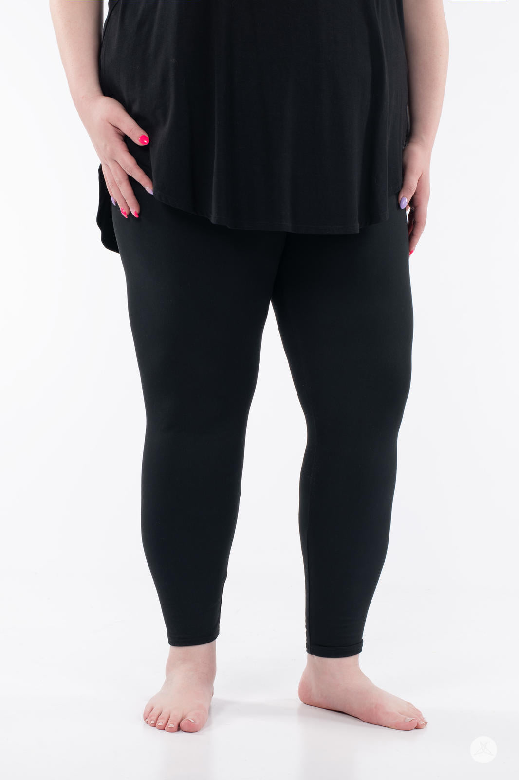 Close-up of an adult wearing SweetLegs Black Licorice leggings with a black top standing barefoot on white background