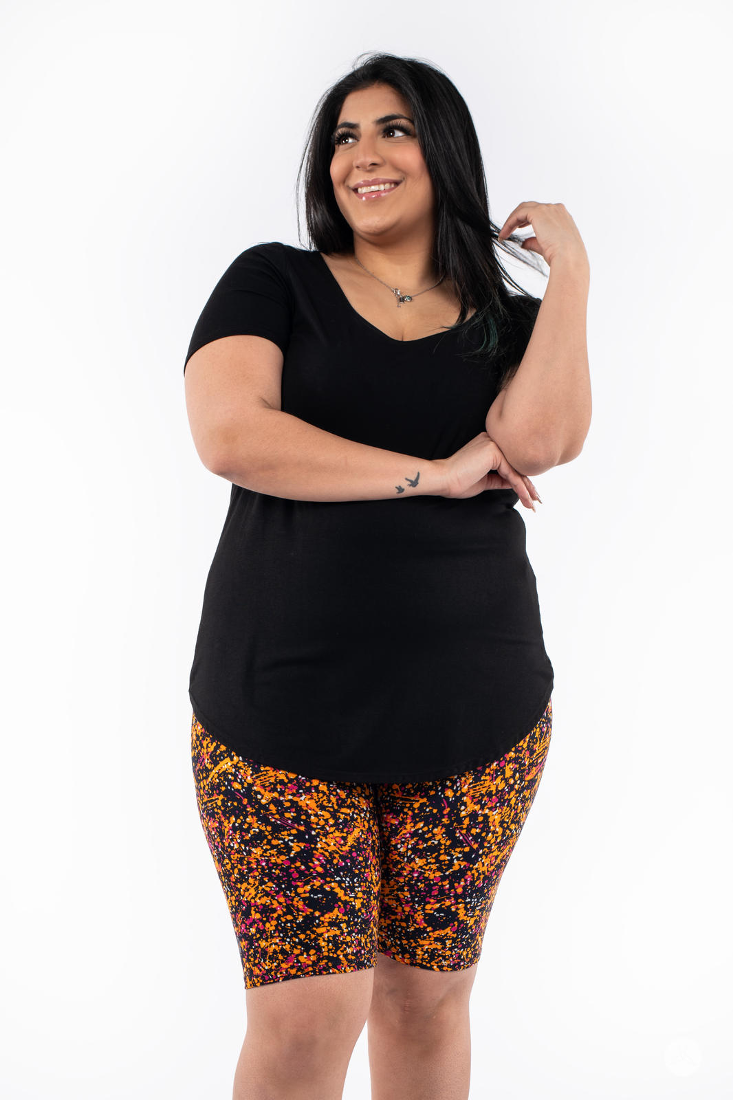 Smiling woman wearing SweetLegs Splatterday Night Biker Shorts with vibrant black, orange, and pink splatter pattern and black top