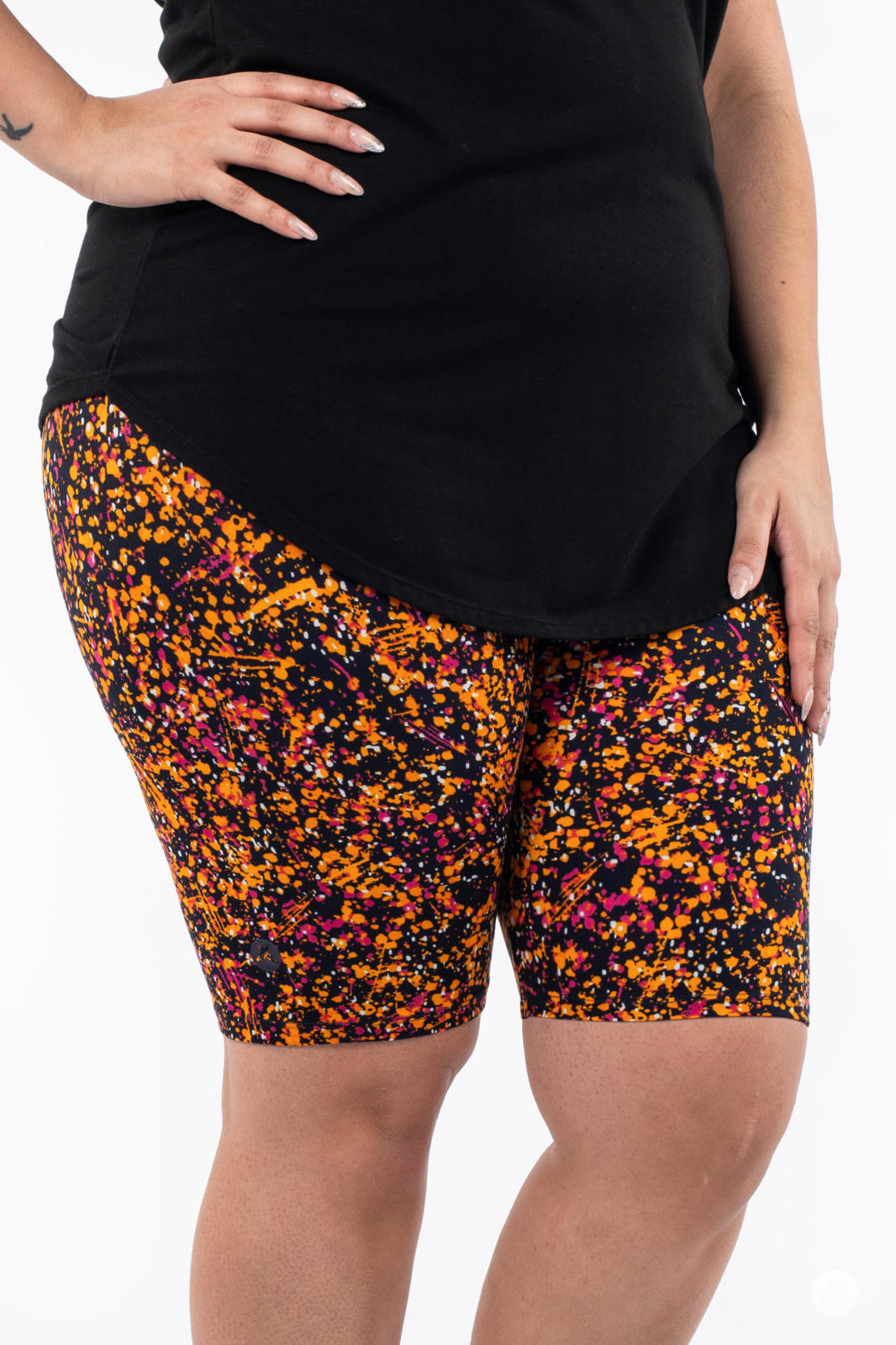 Close-up of person wearing SweetLegs Splatterday Night Biker Shorts in vibrant orange, pink, and black splatter pattern with black top
