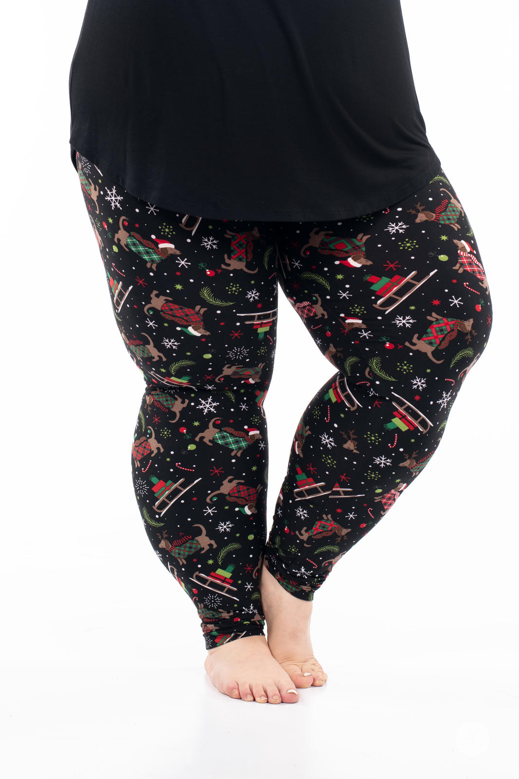 Plus-size legs wearing SweetLegs Happy Pawlidays leggings with festive dachshunds, sleighs, and snowflakes on black background