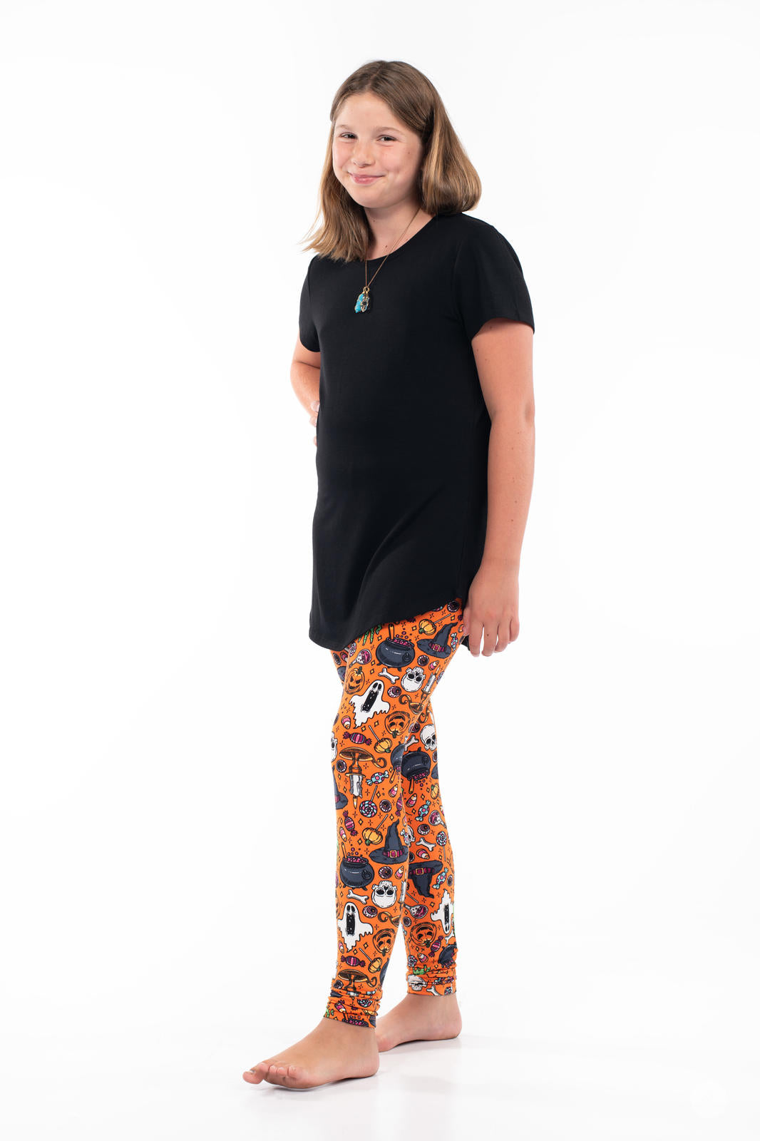 Child wearing SweetLegs Treats No Tricks Kids leggings with Halloween-themed icons on bright orange background