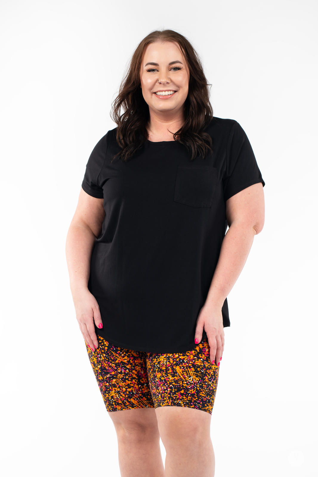 Smiling woman in SweetLegs Splatterday Night Biker Shorts with bright orange and pink splatter pattern and black shirt