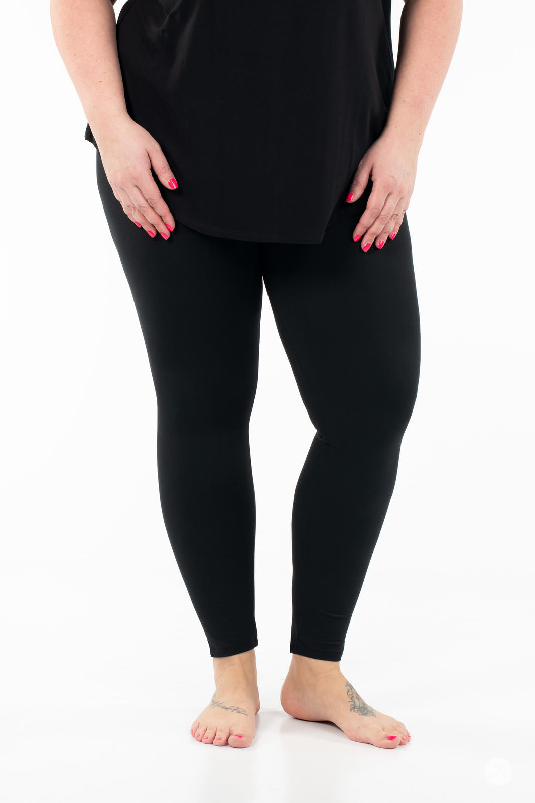 Adult wearing SweetLegs Black Licorice leggings with black top standing barefoot on white background