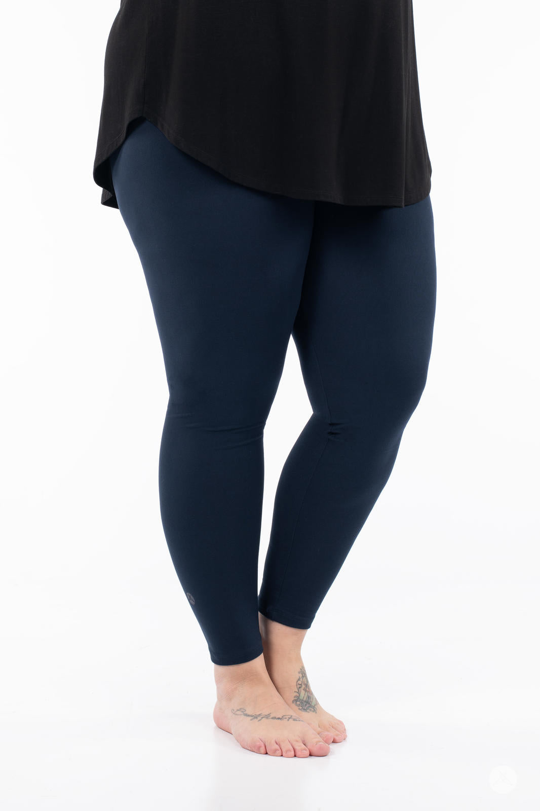 Lower body view of person wearing Navy leggings by SweetLegs paired with black top barefoot on white background