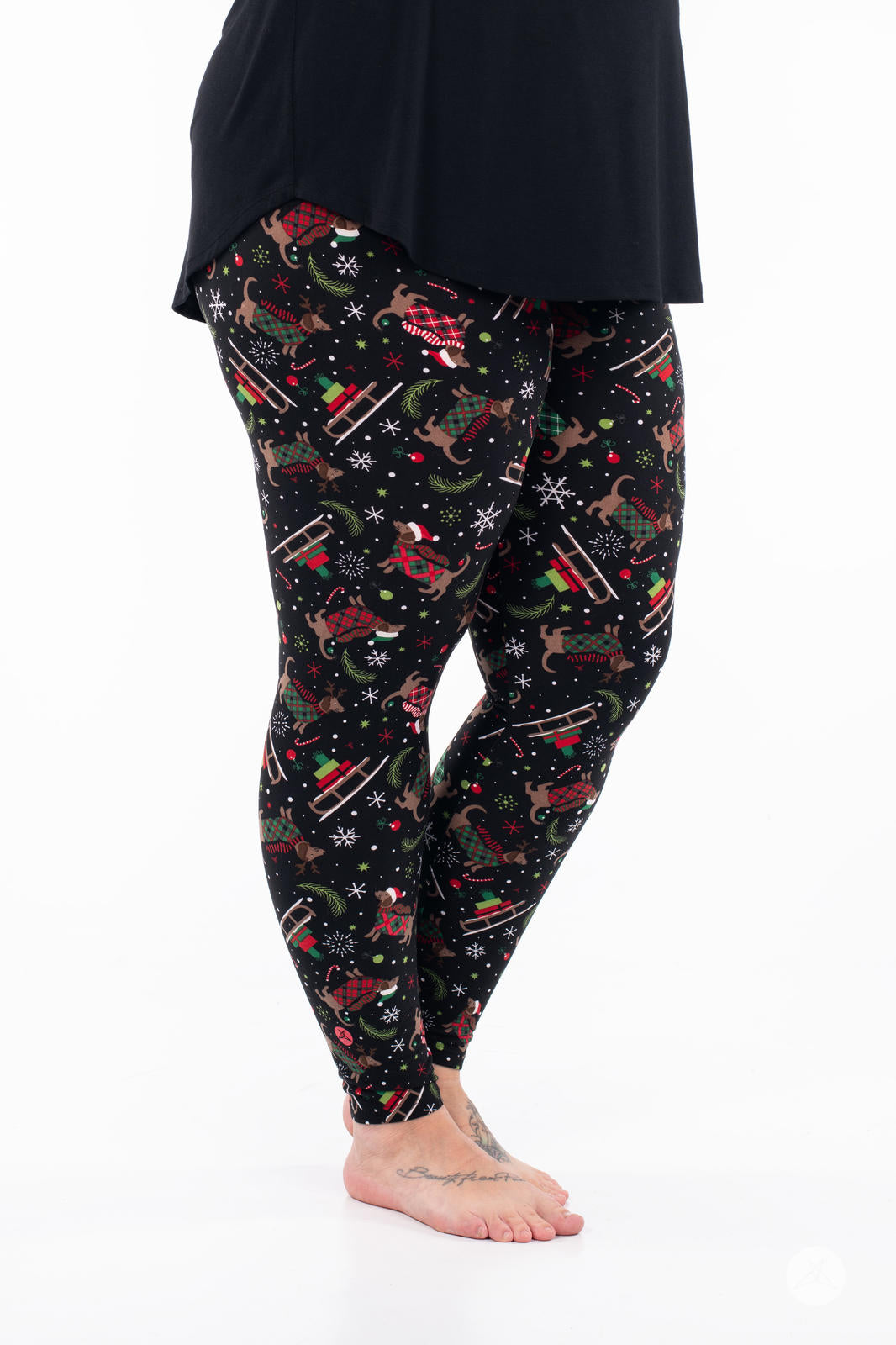 Adult wearing SweetLegs Happy Pawlidays leggings featuring festive Dachshunds in holiday gear and sleighs on black background