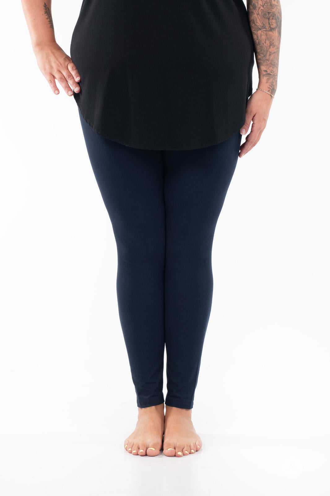 Lower body of person wearing Navy leggings by SweetLegs paired with black top standing barefoot on white background
