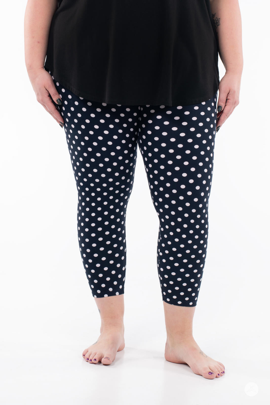Front view of SweetLegs Get Spotted Crops navy polka dot leggings worn with black top on white background