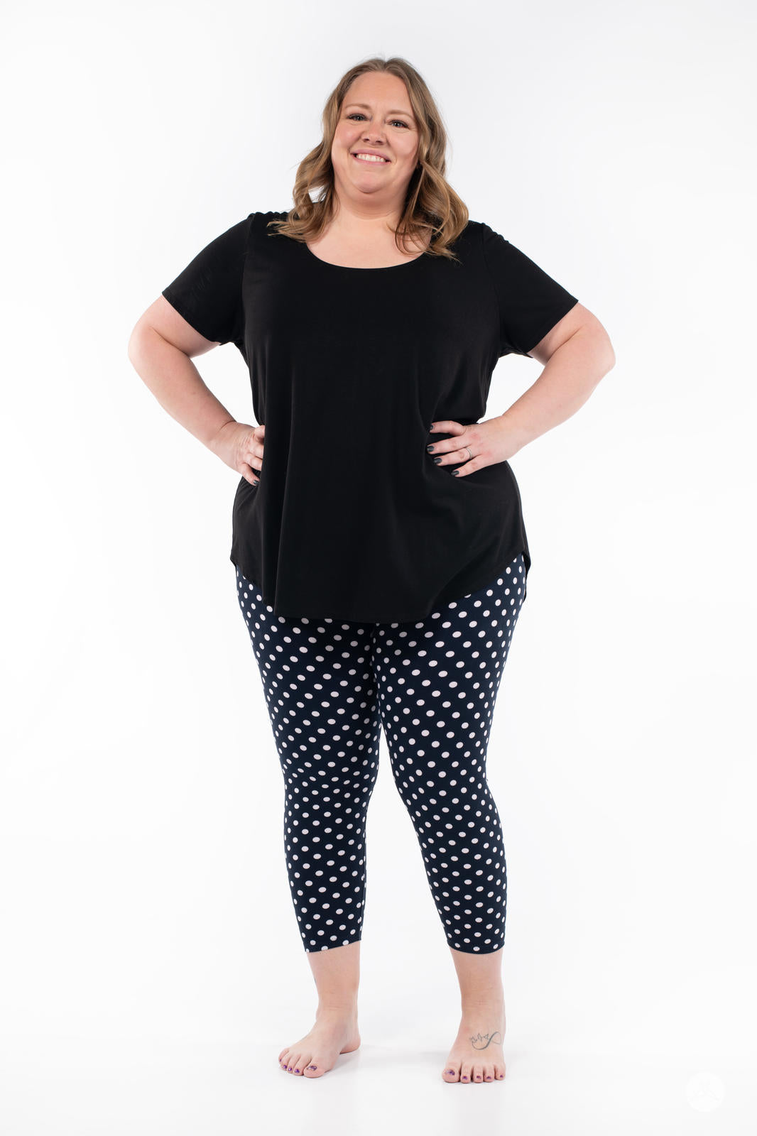 Smiling woman wearing SweetLegs Get Spotted Crops navy polka dot leggings with black top on white background