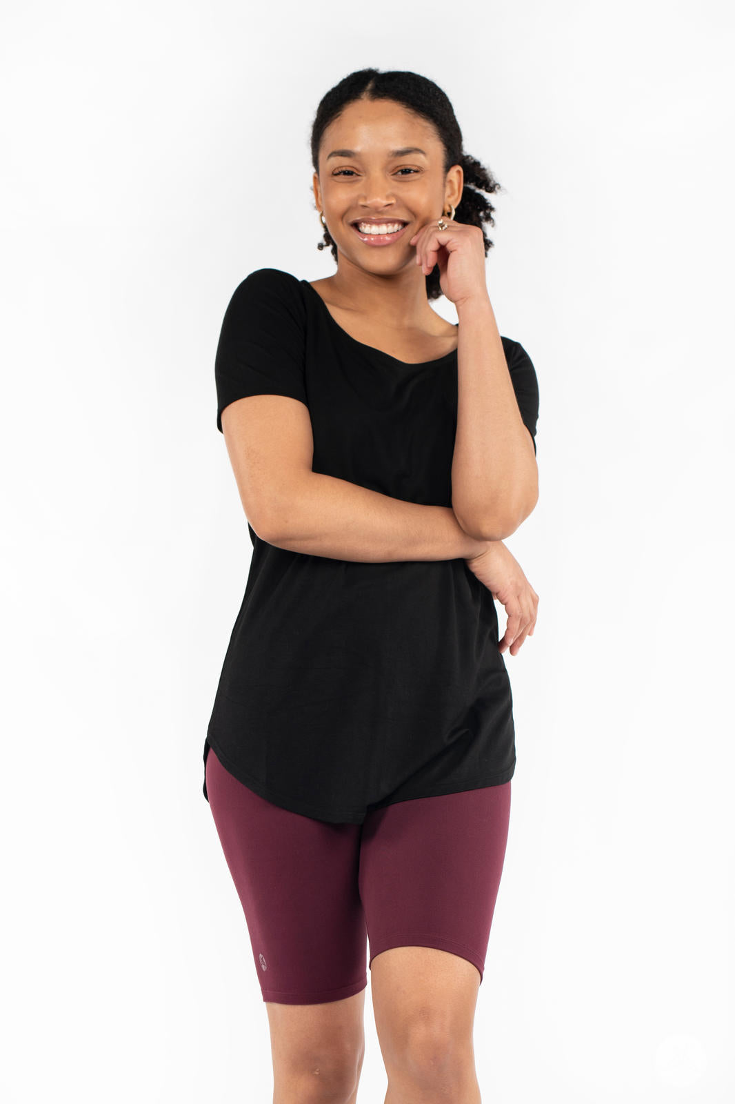 Smiling model wearing SweetLegs Mulberry Biker Shorts in deep maroon paired with black short sleeve top on white background