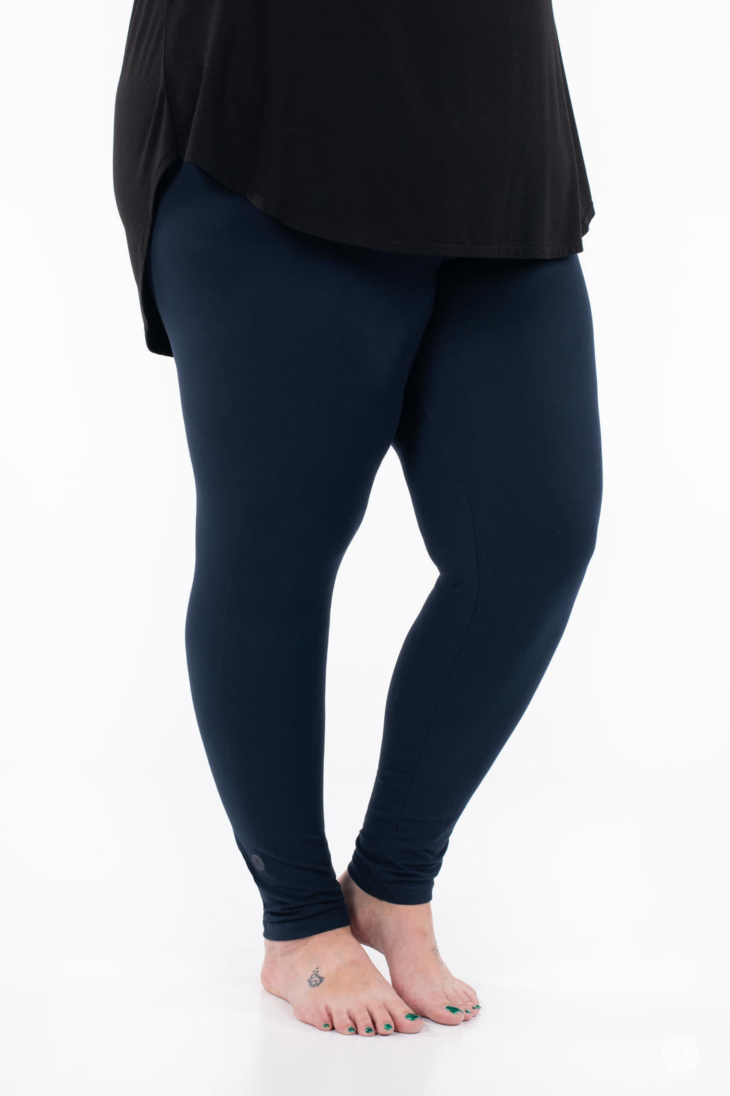 Legs view of person wearing Navy leggings by SweetLegs paired with a black top standing barefoot on white background