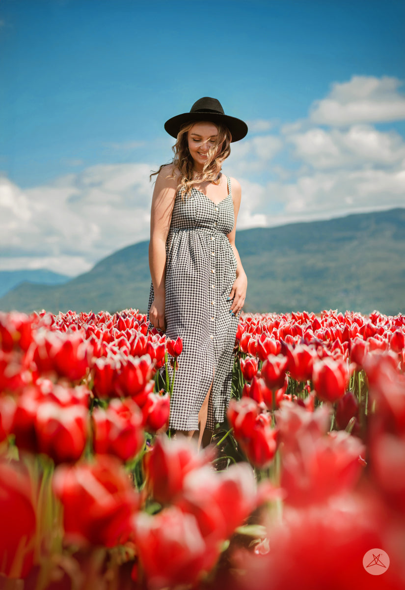 Woman in black and white SweetTops Gingham Dress with buttons and adjustable straps standing in red tulip field