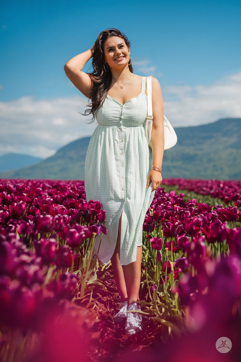 Woman wearing SweetTops Gingham Dress in soft green with button front, standing in vibrant field of purple flowers outdoors