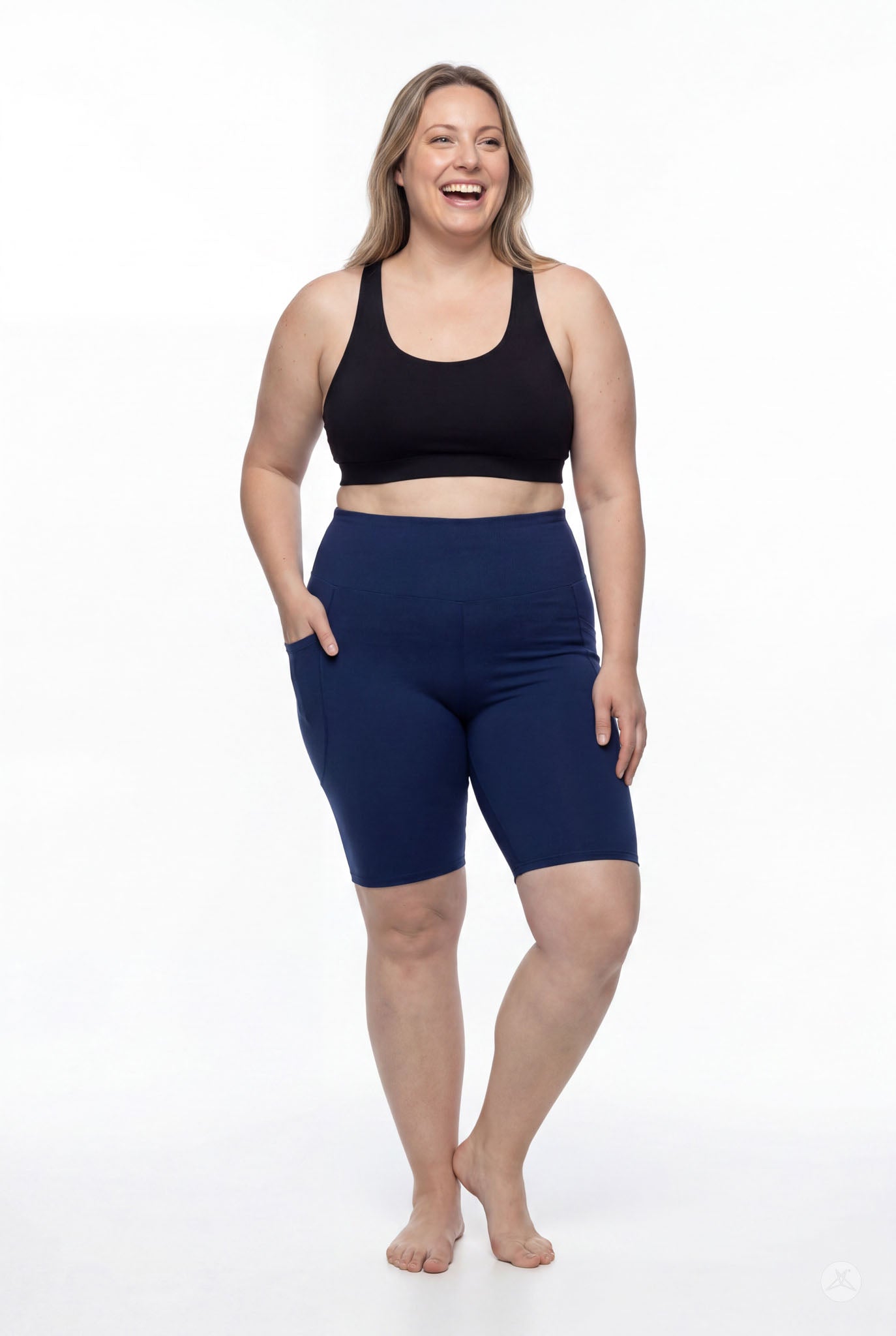 Smiling woman wearing SweetLegs Still Water High-Waisted Pocket Biker Shorts in navy with side pockets and black sports bra