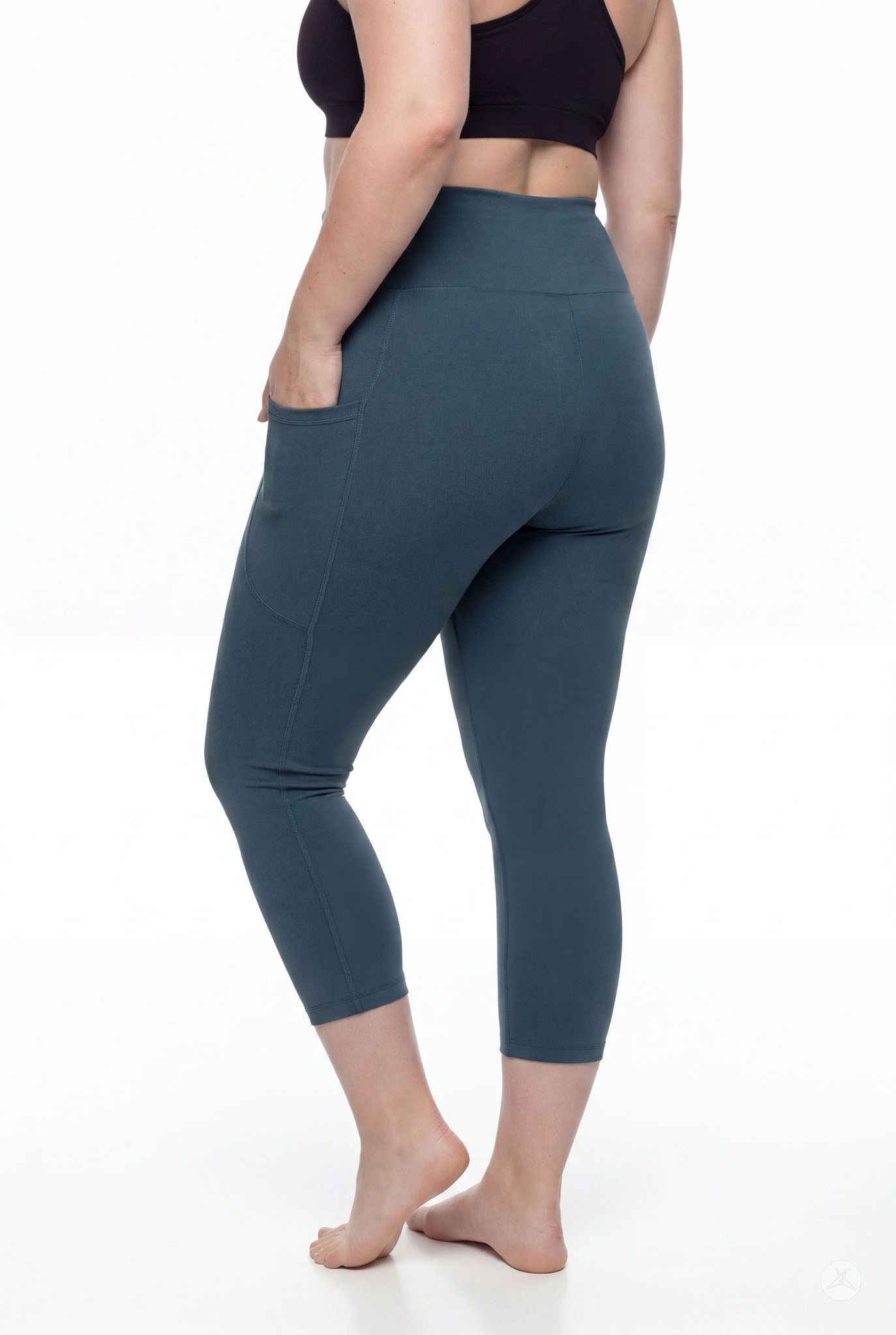 Woman standing barefoot wearing SweetLegs Deep Teal High-Waisted Pocket Crops with hand in side pocket back view