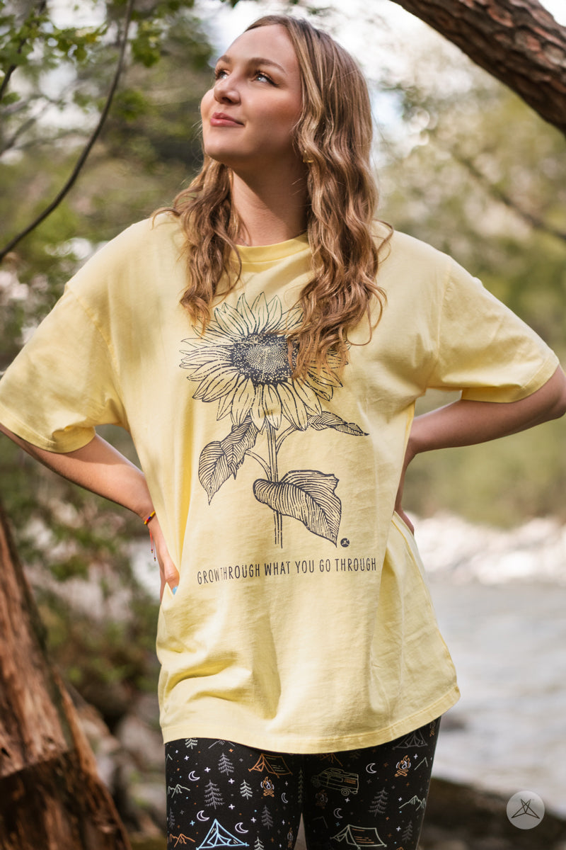 Woman outdoors wearing SweetTops Vintage Graphic Tee in pale yellow with sunflower and inspirational growth affirmation text