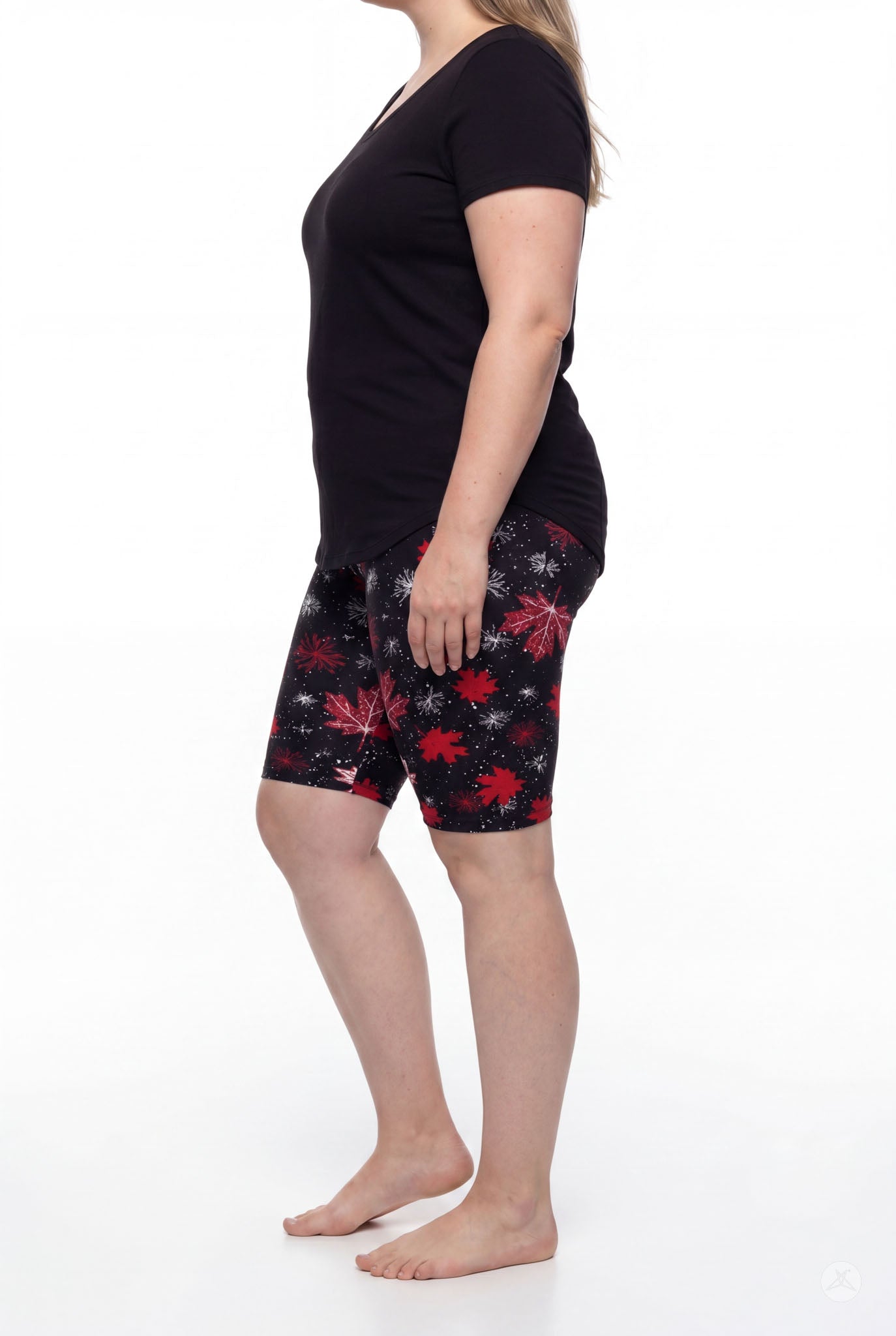 Side view of woman standing barefoot wearing SweetLegs Maple Mood Biker Shorts with red maple leaf pattern and black top