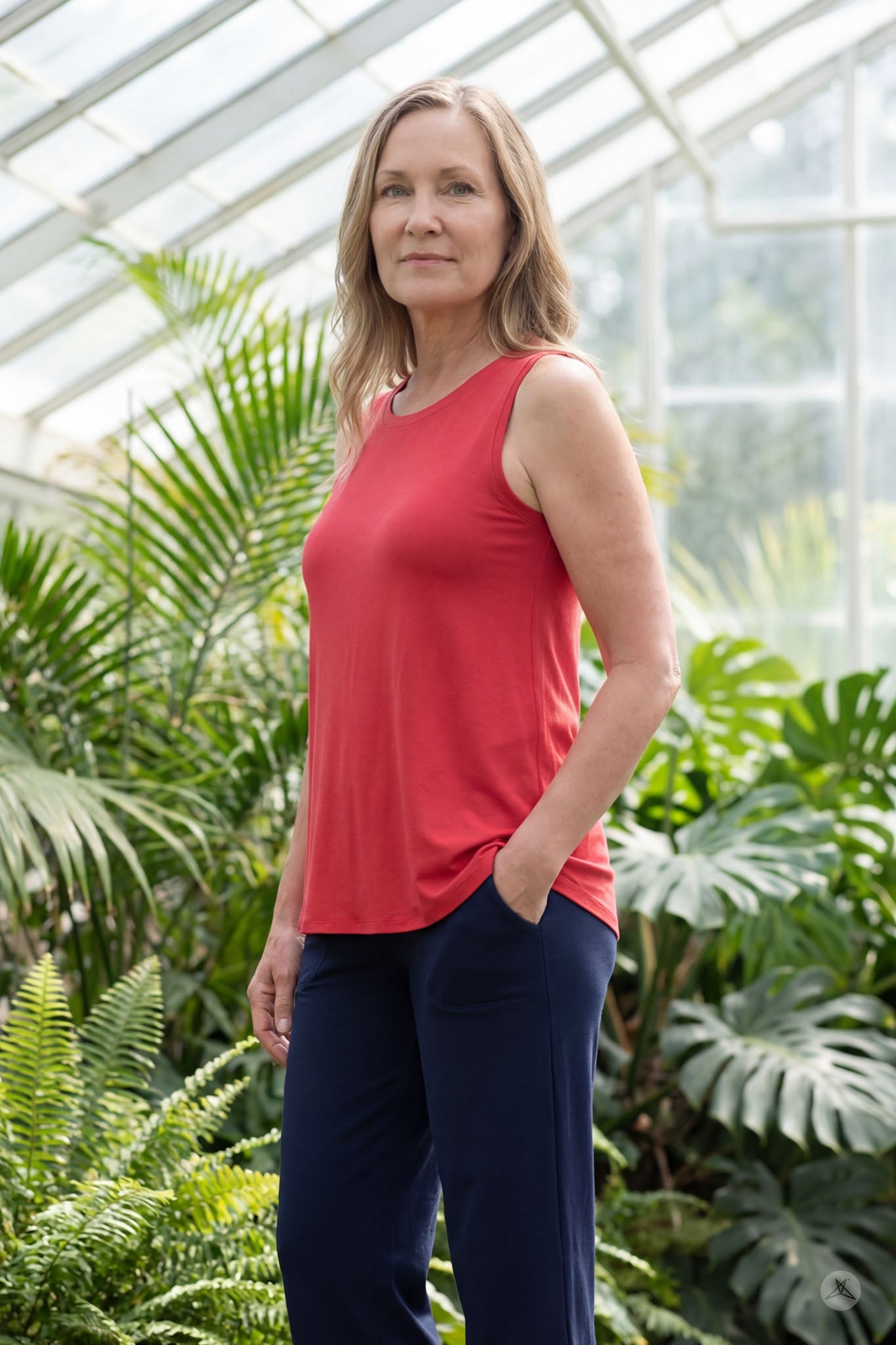 Woman standing in greenhouse wearing red sleeveless High Neck Tank by sweettops with hands in pockets