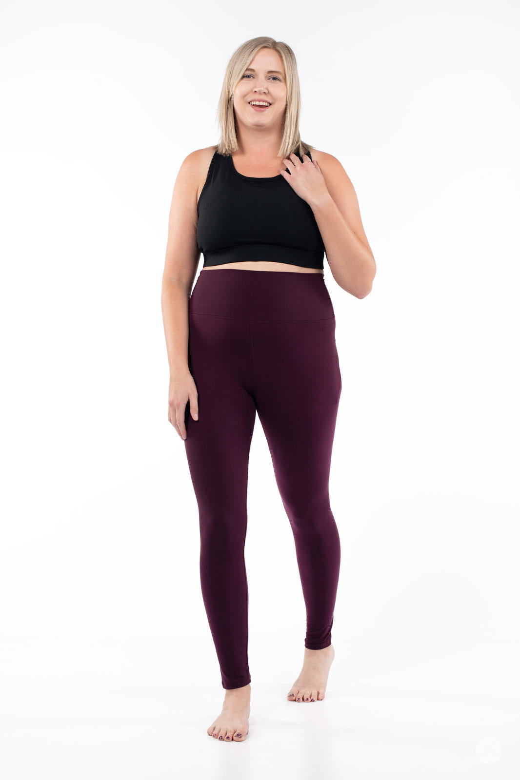 Smiling model wearing SweetLegs Blackberry High-Waisted Leggings in deep rich purple with black crop top front view barefoot