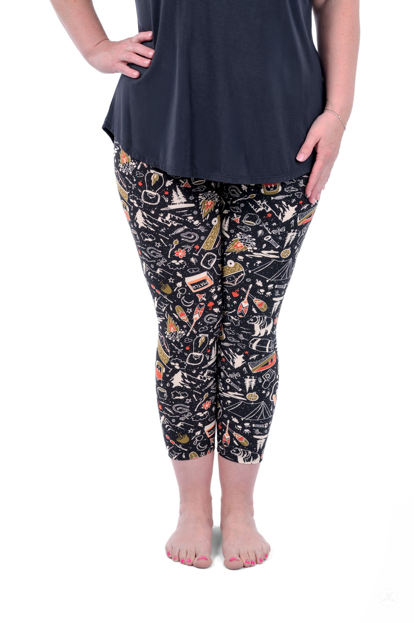 Plus size model wearing SweetLegs Off Grid Crops with black camping-themed pattern and black top standing barefoot front view