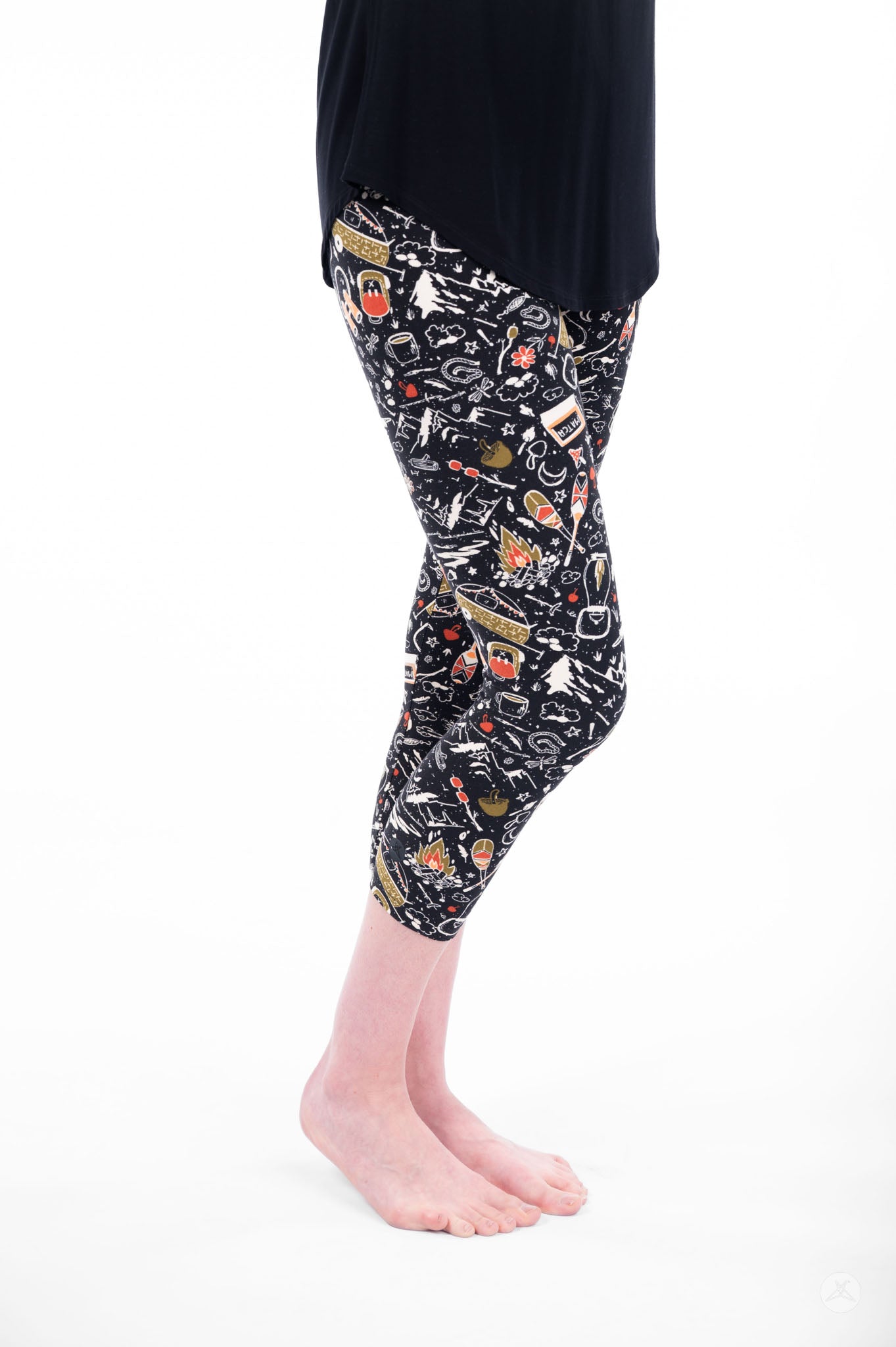 Person wearing SweetLegs Off Grid Crops with camping-themed pattern in black standing barefoot side view