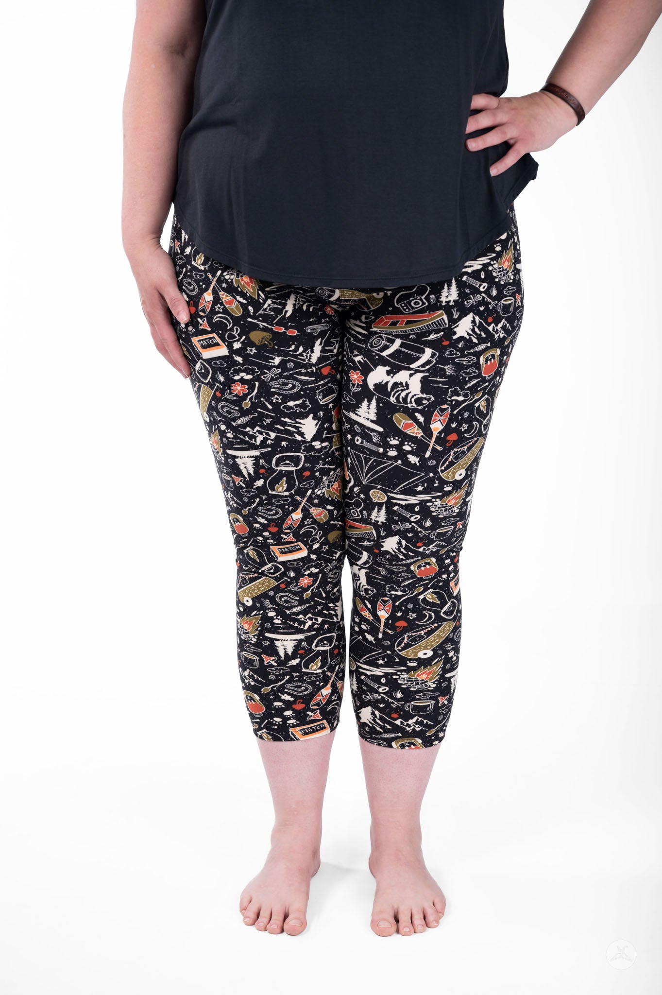Plus size woman wearing SweetLegs Off Grid Crops with black camping pattern and black top standing barefoot front view