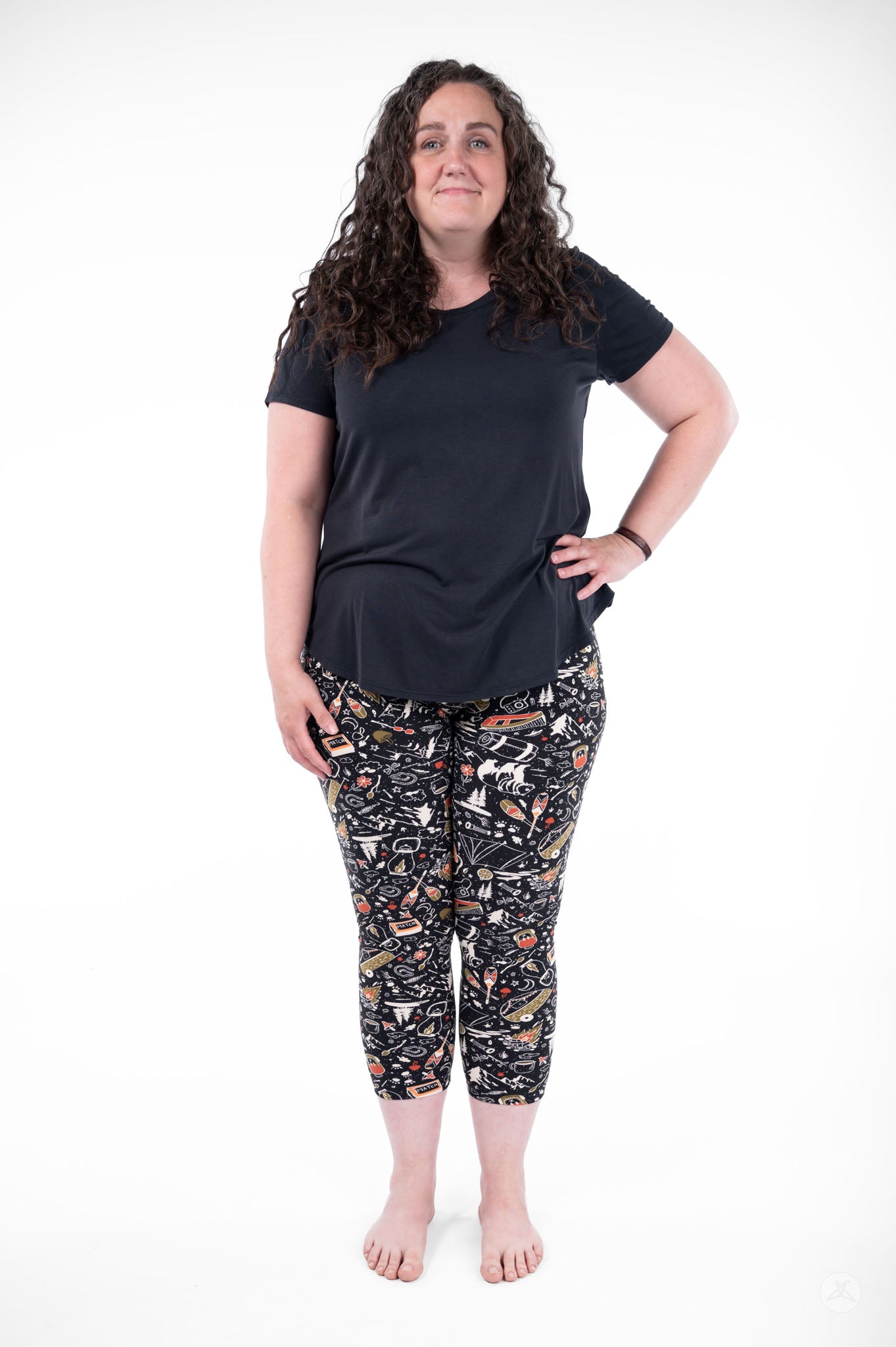 Plus size woman standing barefoot wearing SweetLegs Off Grid Crops with outdoor pattern and black top front view