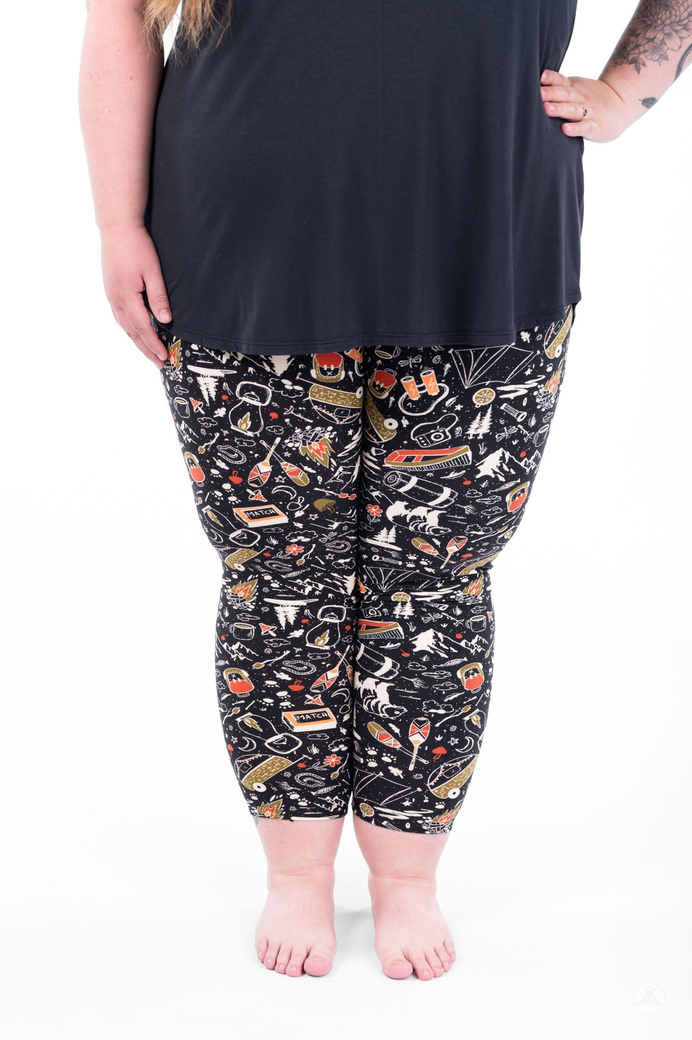 Plus size woman wearing SweetLegs Off Grid Crops with black camping pattern standing barefoot front view