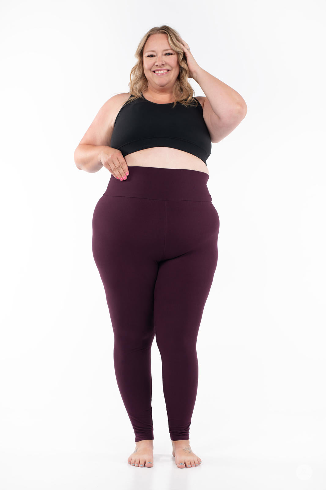 Plus-size model wearing SweetLegs Blackberry High-Waisted Leggings in deep rich purple front view barefoot with black sports bra