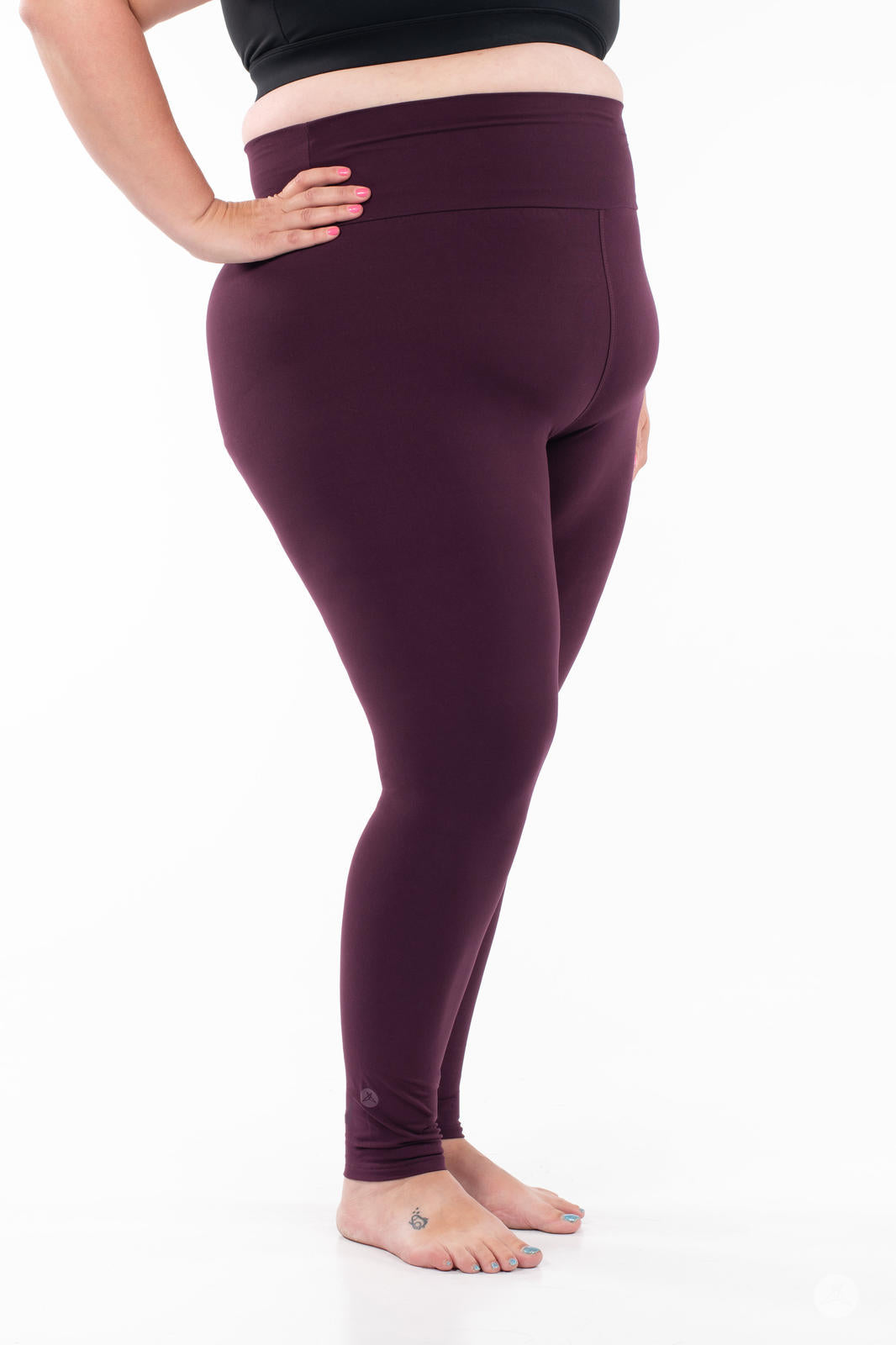 Plus-size model wearing SweetLegs Blackberry High-Waisted Leggings in deep rich purple side view barefoot with black top
