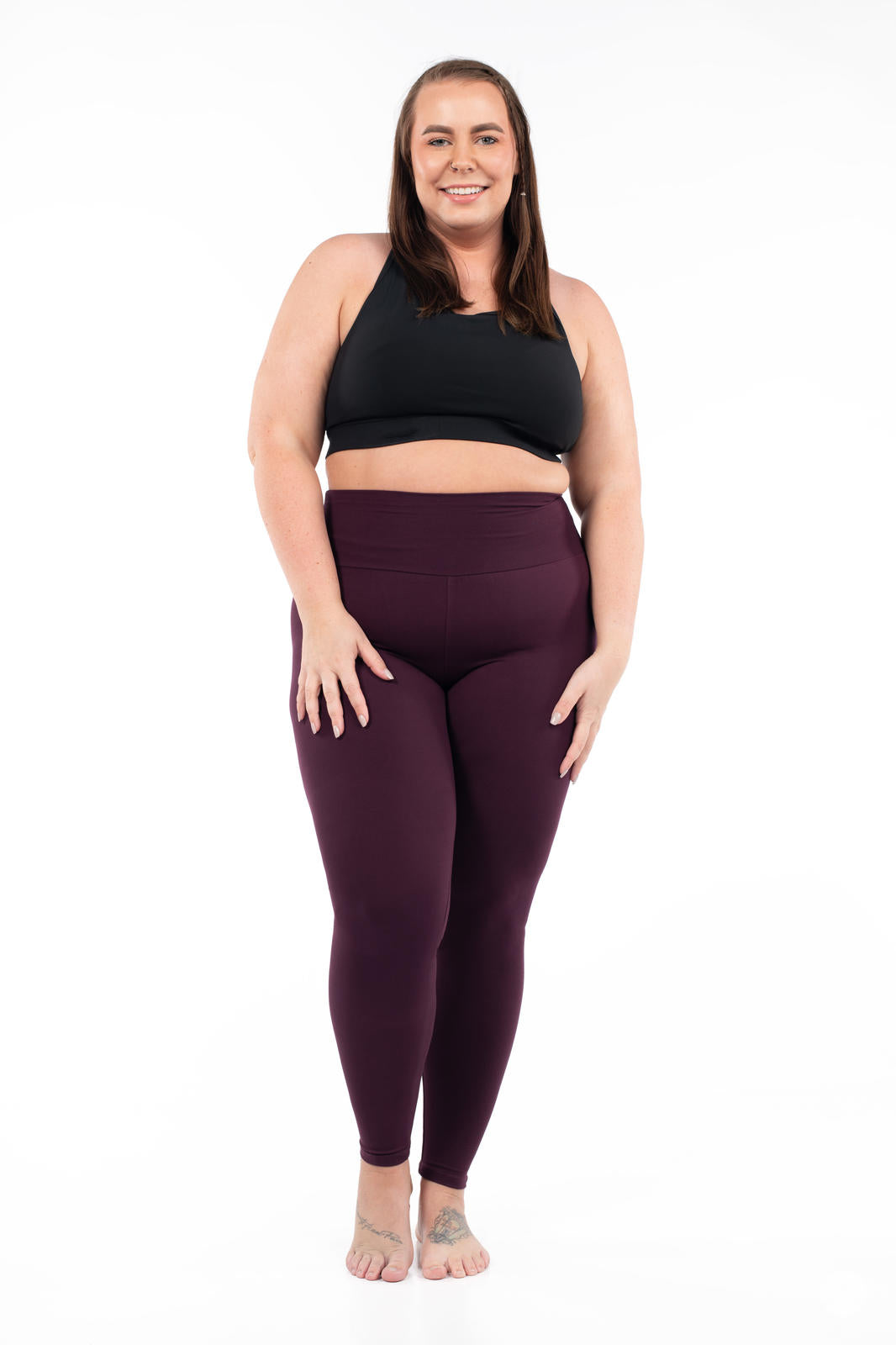 Plus-size model standing barefoot wearing SweetLegs Blackberry High-Waisted Leggings paired with a black crop top front view