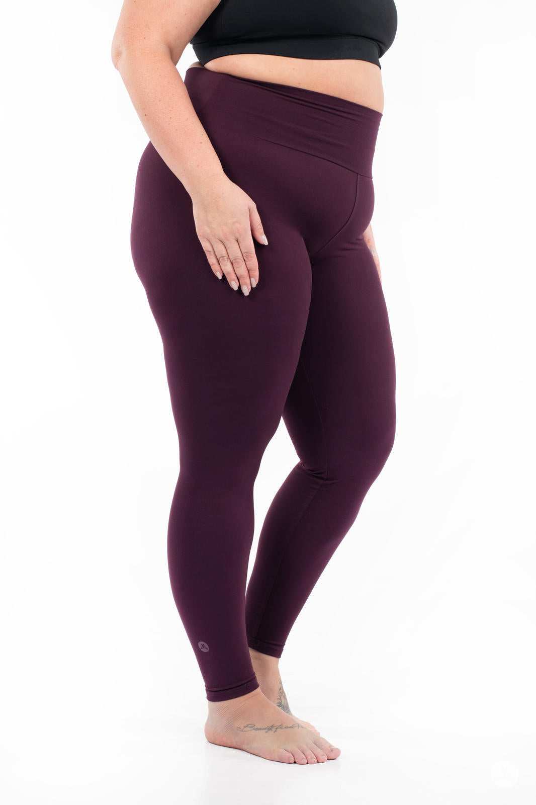 Plus-size model wearing SweetLegs Blackberry High-Waisted Leggings in deep rich purple side view barefoot with black crop top