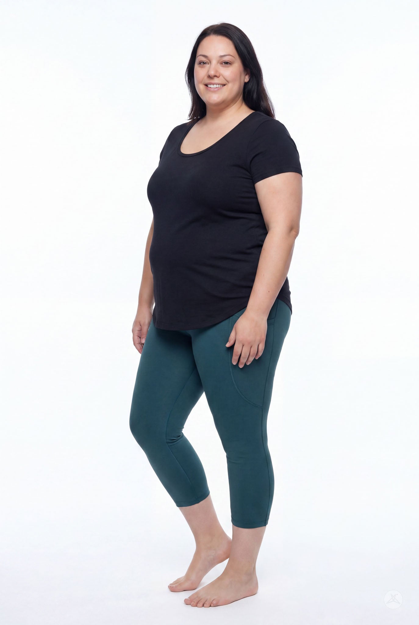 Plus size model wearing SweetLegs Deep Teal Pocket Crops leggings with side pockets and black top standing barefoot side view