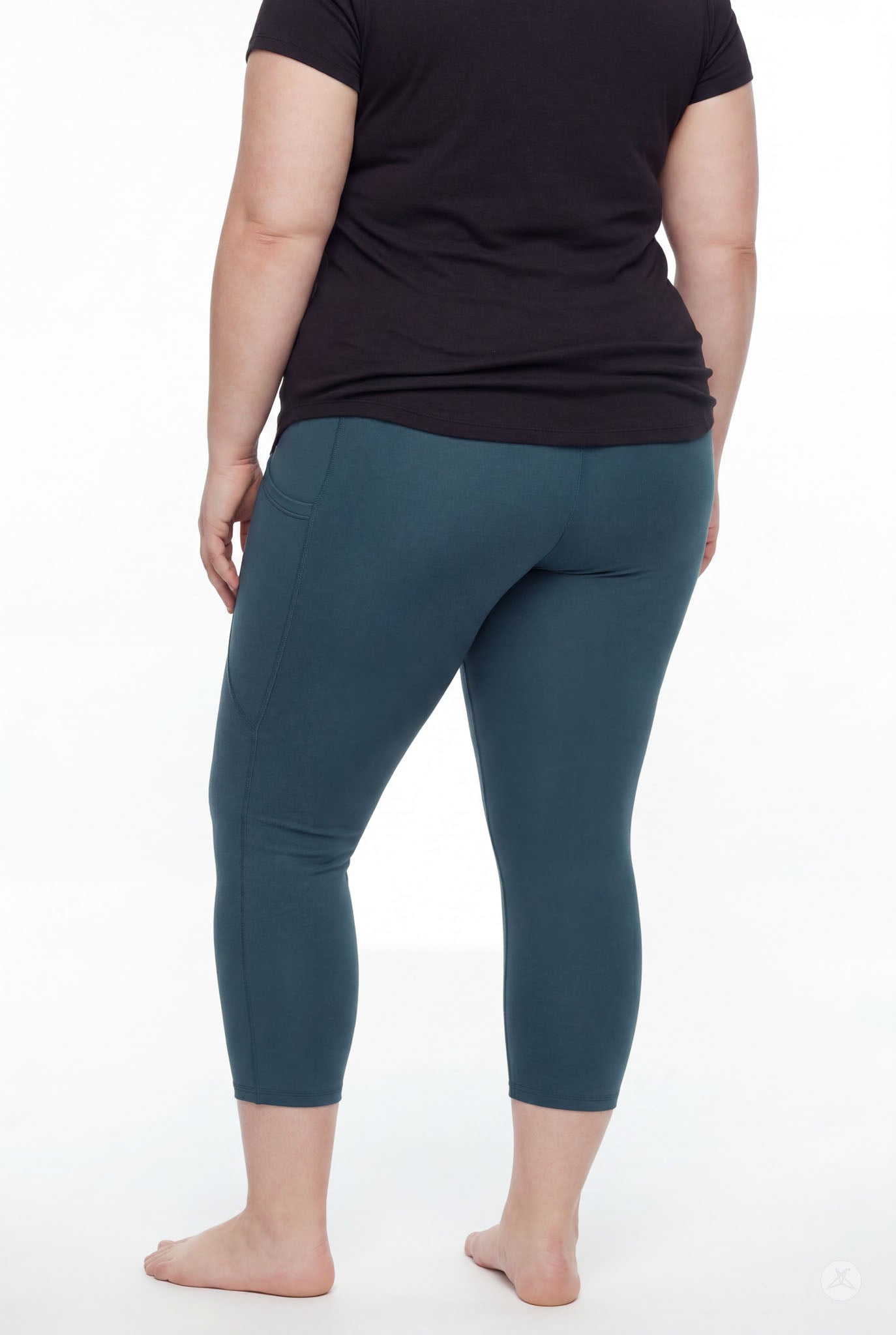 Plus size woman wearing SweetLegs Deep Teal Pocket Crops leggings standing barefoot beside white background back view