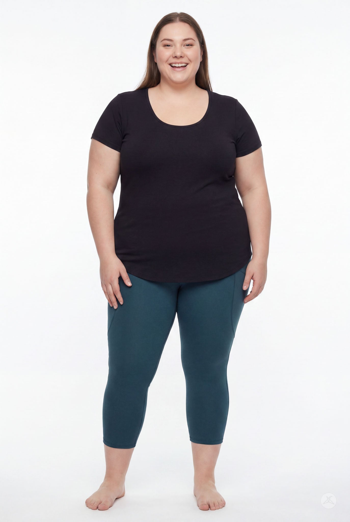 Plus size woman smiling barefoot wearing SweetLegs Deep Teal Pocket Crops leggings and black scoop neck top front view
