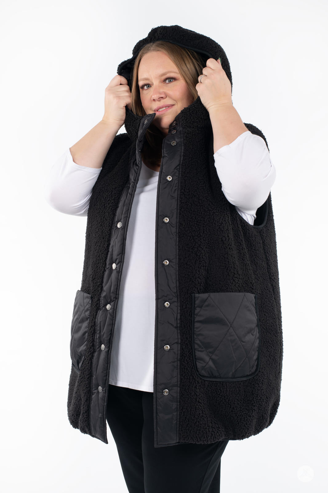 Plus-size woman wearing SweetLegs Canada Reversible Quilted Sherpa Vest in black adjusting the hood with snap buttons visible