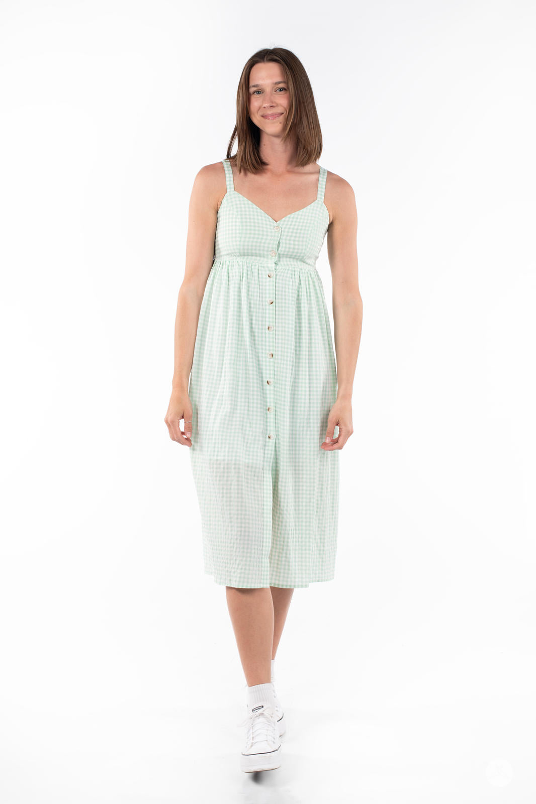 Woman smiling and wearing SweetTops Gingham Dress in light green with button front and adjustable straps on white background