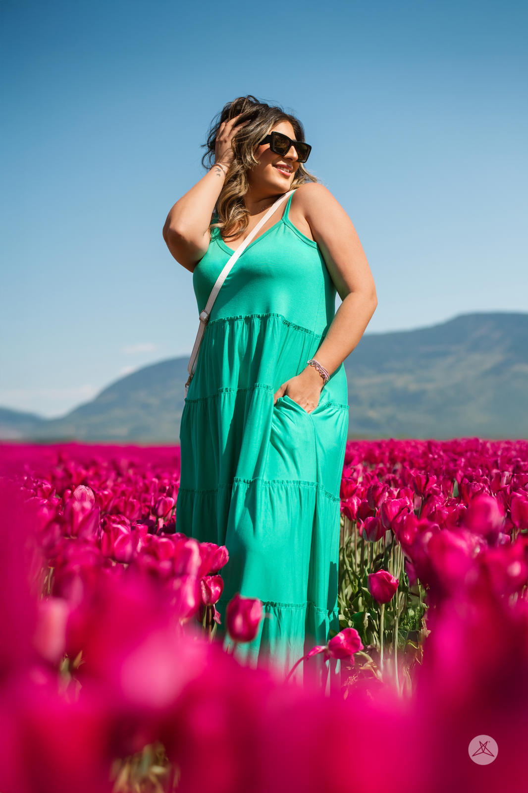 Woman wearing SweetTops The Summer Tiered Dress in teal among bright pink flowers with mountains in the background