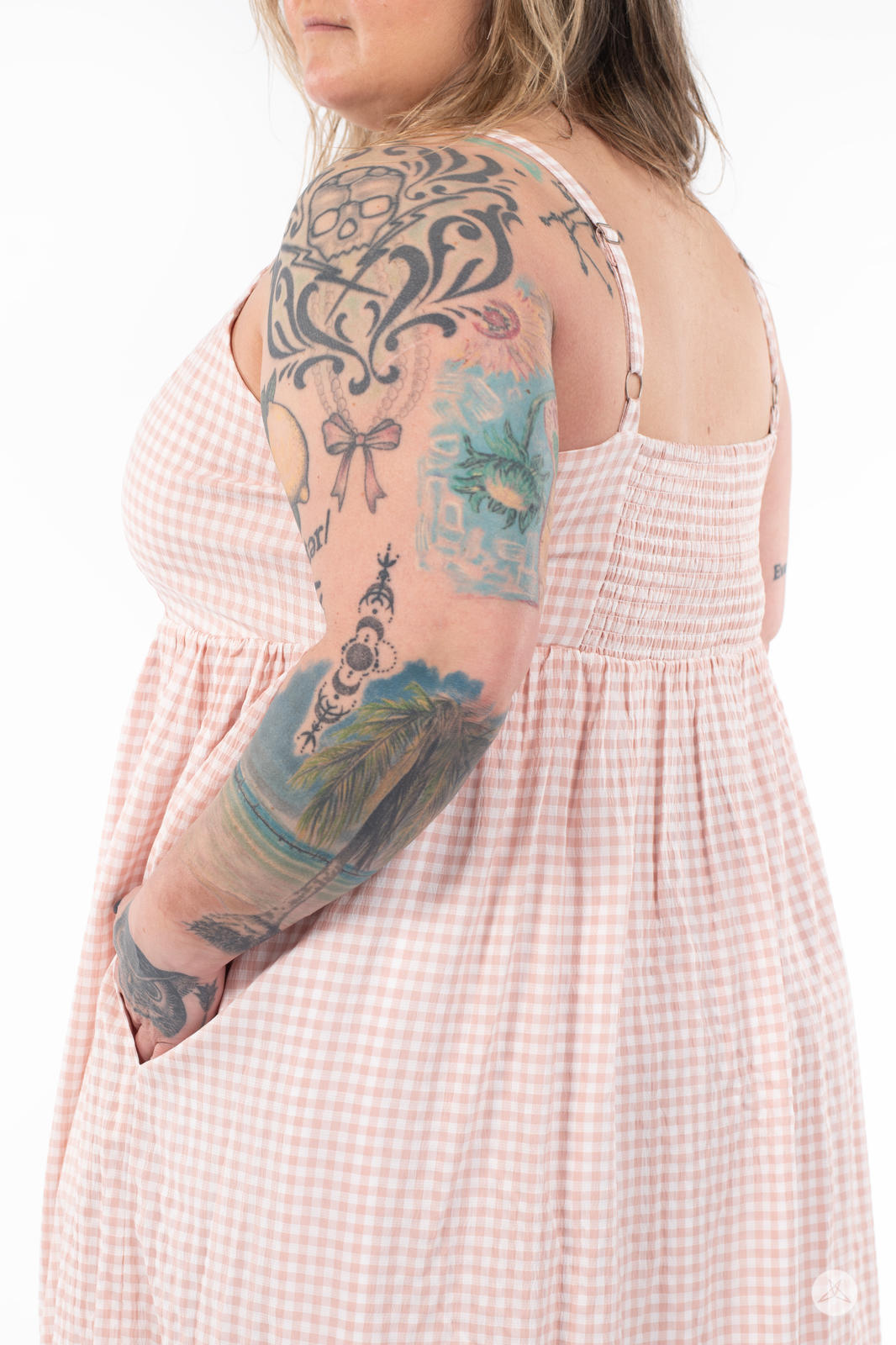 Plus-size model wearing SweetTops Gingham Dress in soft pink with adjustable straps and side pocket visible from back angle