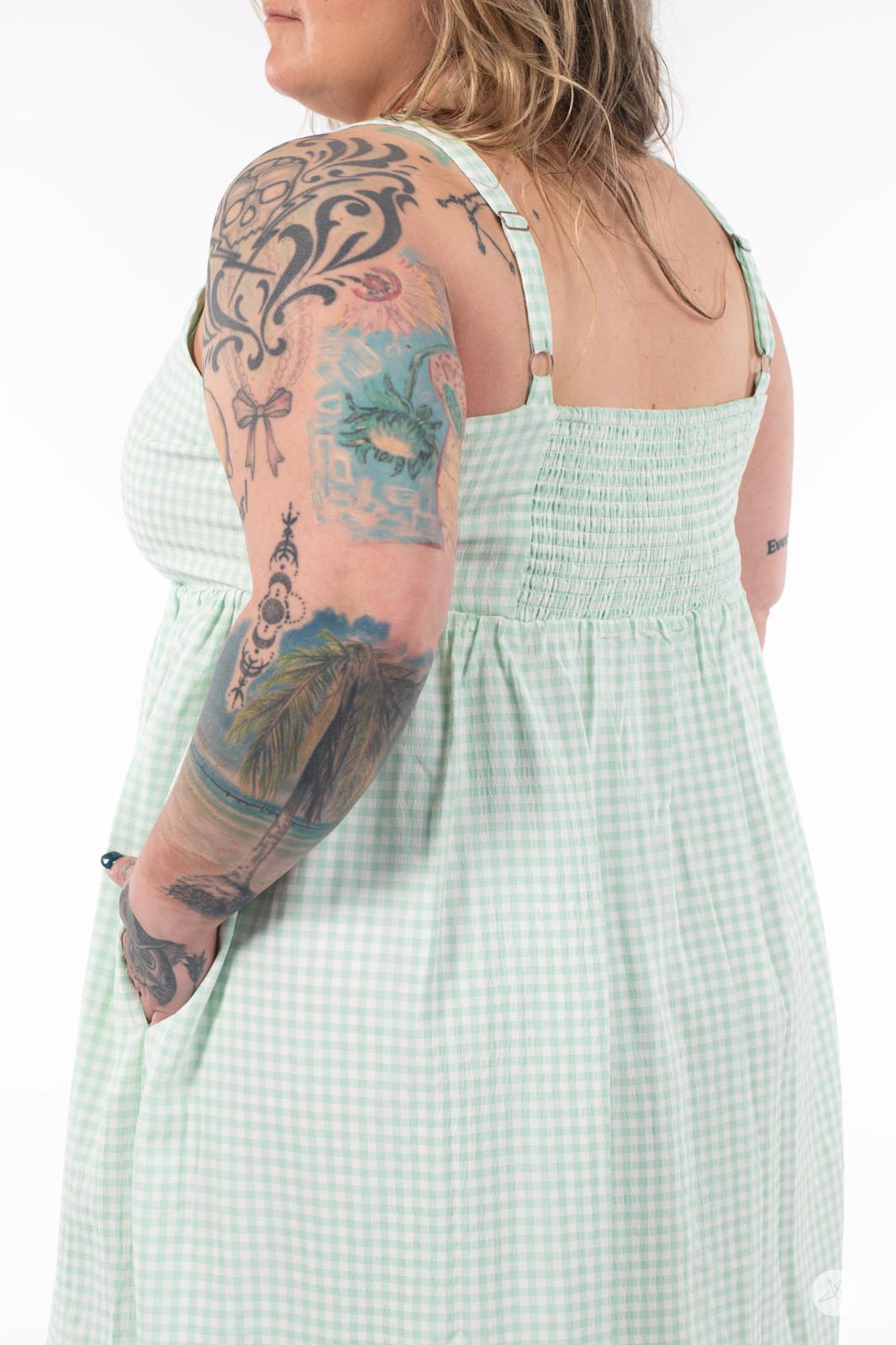 Plus-size model showing back view of SweetTops Gingham Dress in soft green with adjustable straps and gathered bodice
