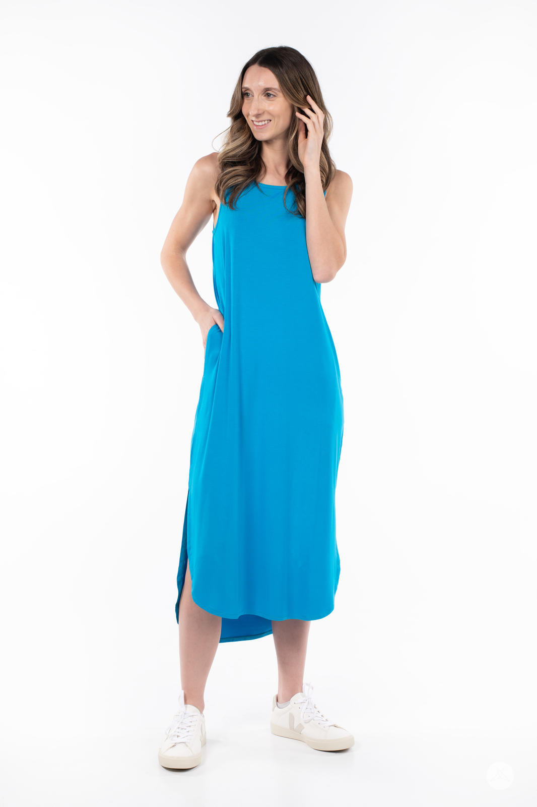Woman smiling wearing SweetTops Sleeveless Tank Dress in bright blue with pockets and side slit paired with white sneakers