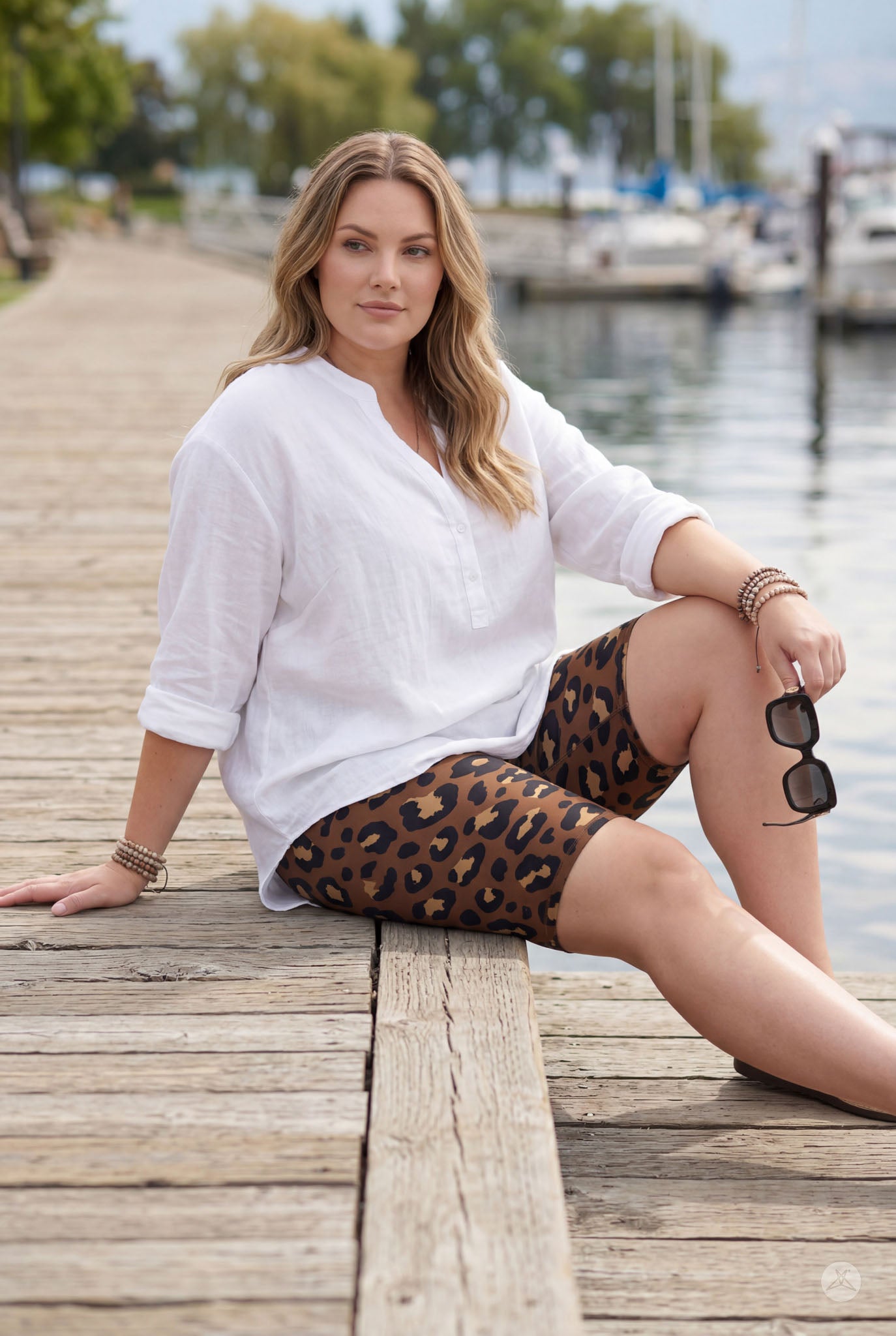 Woman sitting on dock by water wearing SweetLegs Mocha Spots Biker Shorts with leopard print and white top