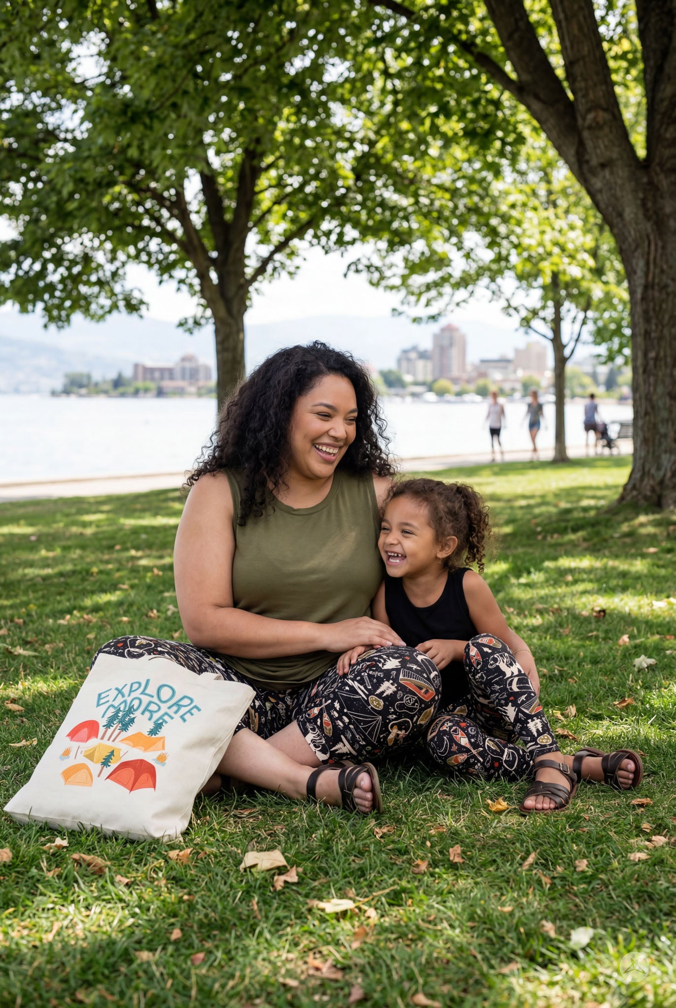 Smiling mother and child sitting outdoors by water wearing Off Grid Kids leggings by SweetLegs on grass under trees