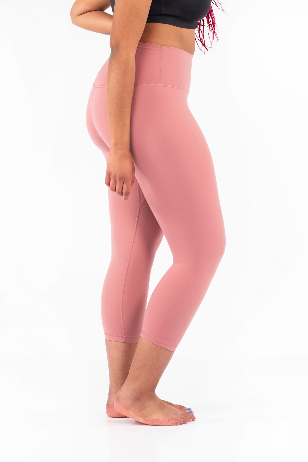 Side view of woman wearing pink Free Motion Crops by Athleisure from SweetLegs collection barefoot on white background
