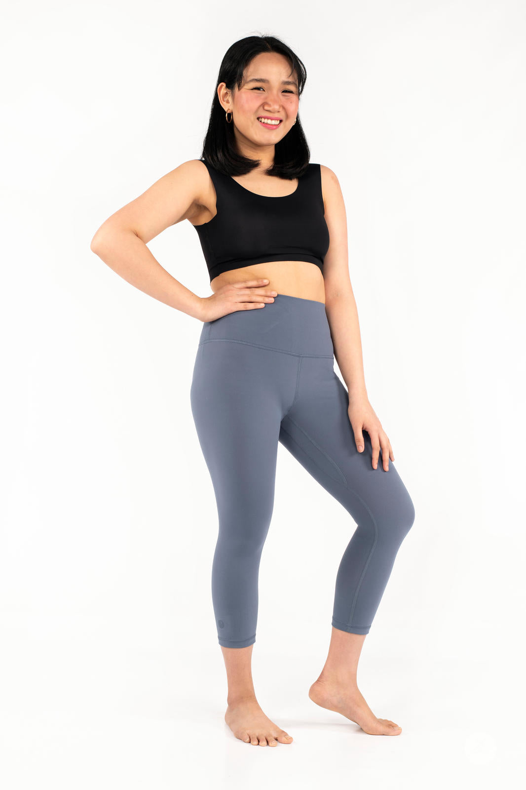 Smiling woman wearing blue Free Motion Crops by Athleisure from SweetLegs collection standing barefoot on white background