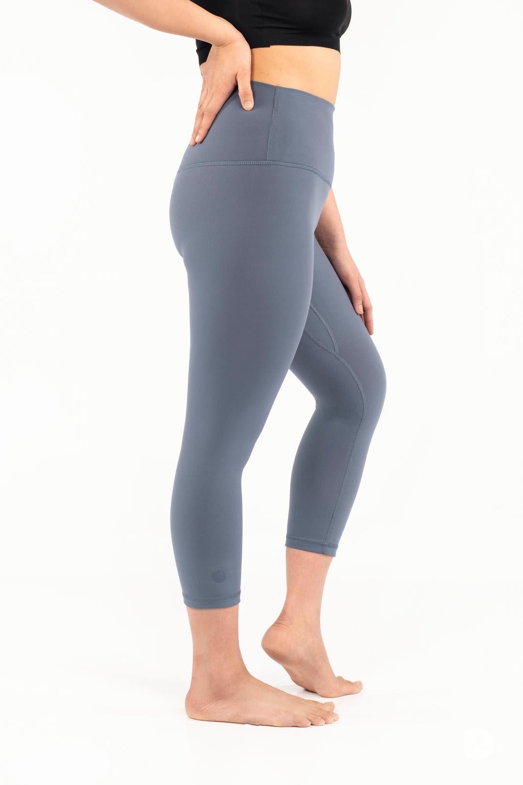 Side view of woman wearing blue-gray Free Motion Crops by Athleisure SweetLegs standing barefoot on white background